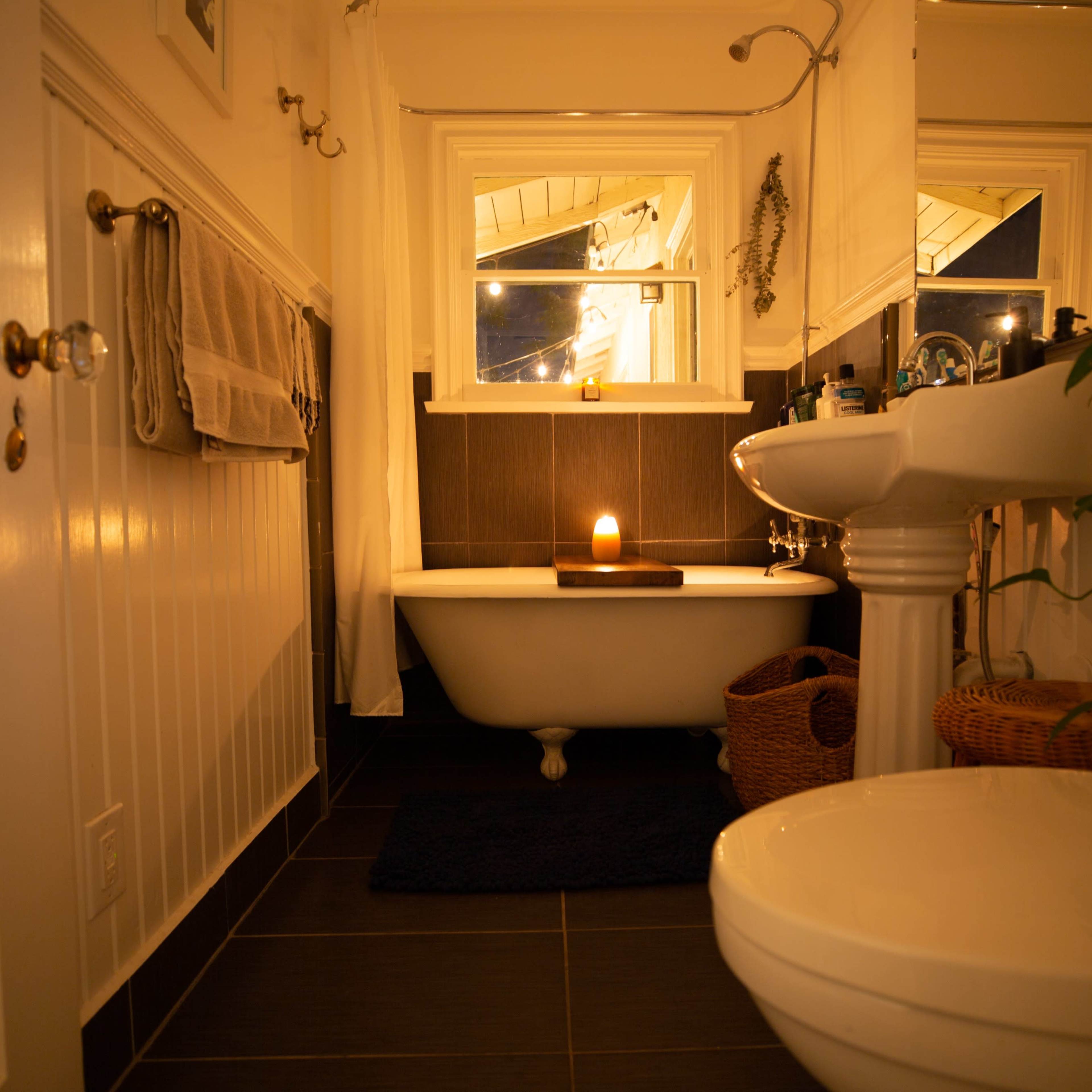 A bathroom with a clawfoot bathtub, a pedestal sink, a toilet, and warm lighting illuminating the space.