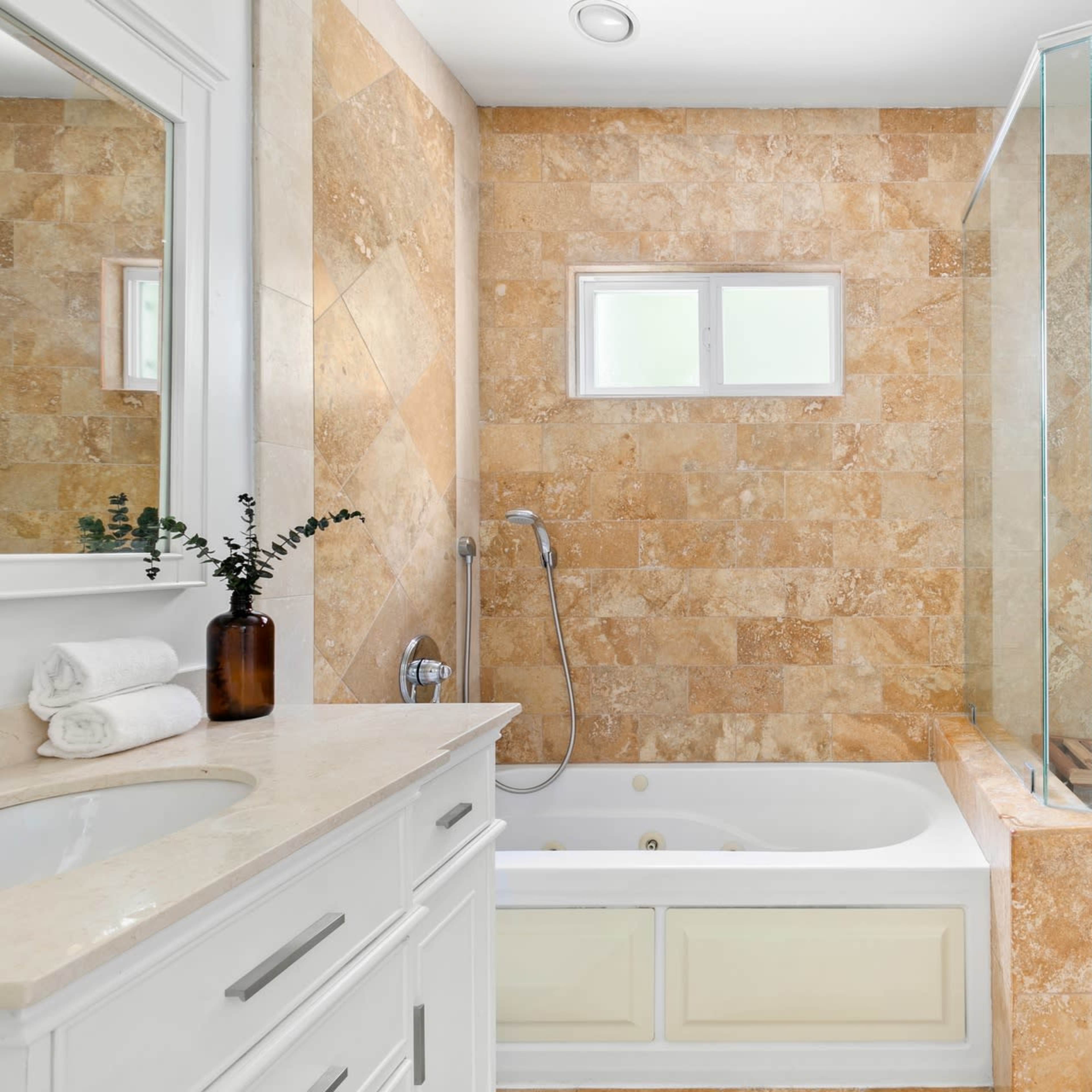 A modern bathroom featuring a glass shower enclosure, a bathtub, and light-colored stone walls.