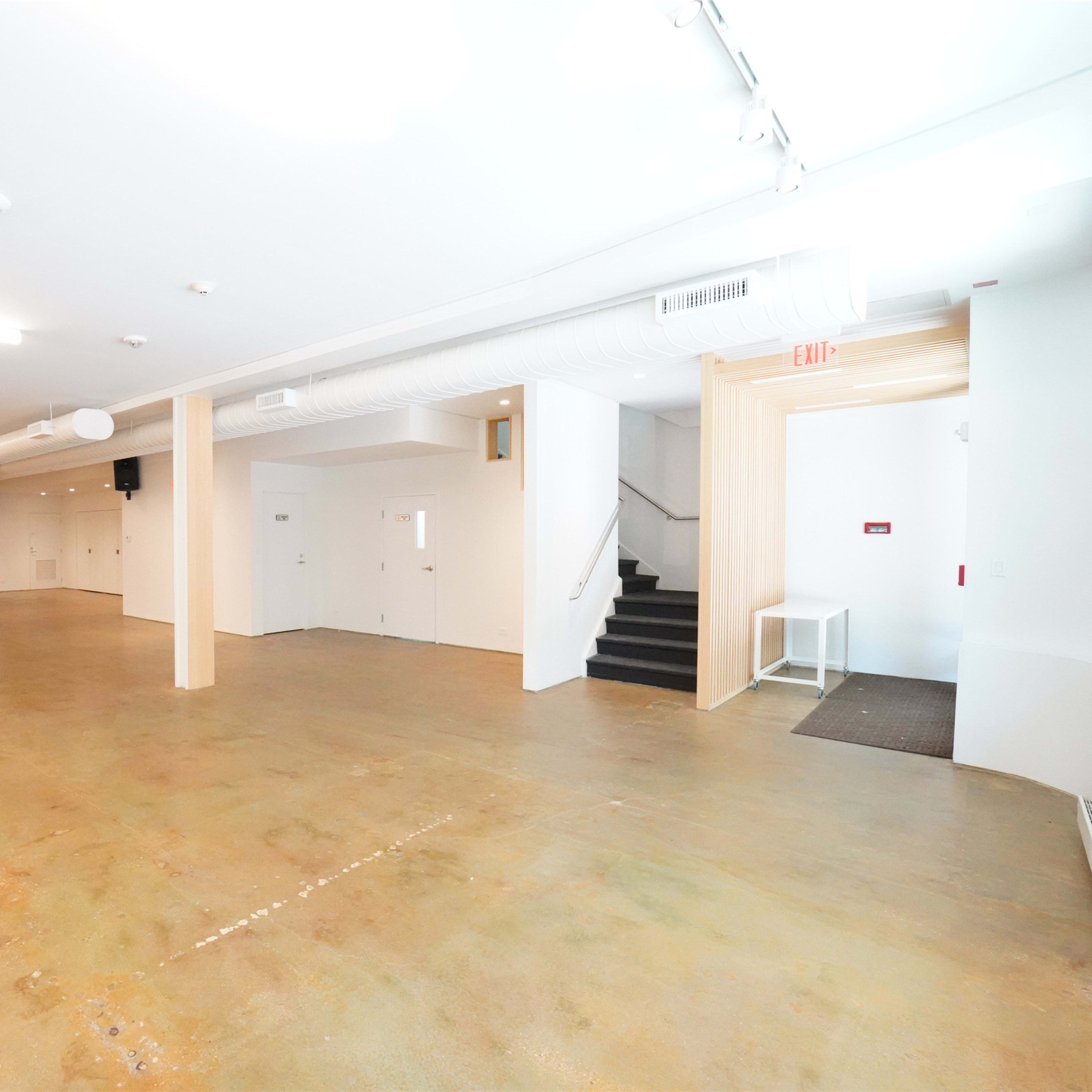 A spacious, empty indoor area with a concrete floor, pale walls, and a staircase leading to a second level.