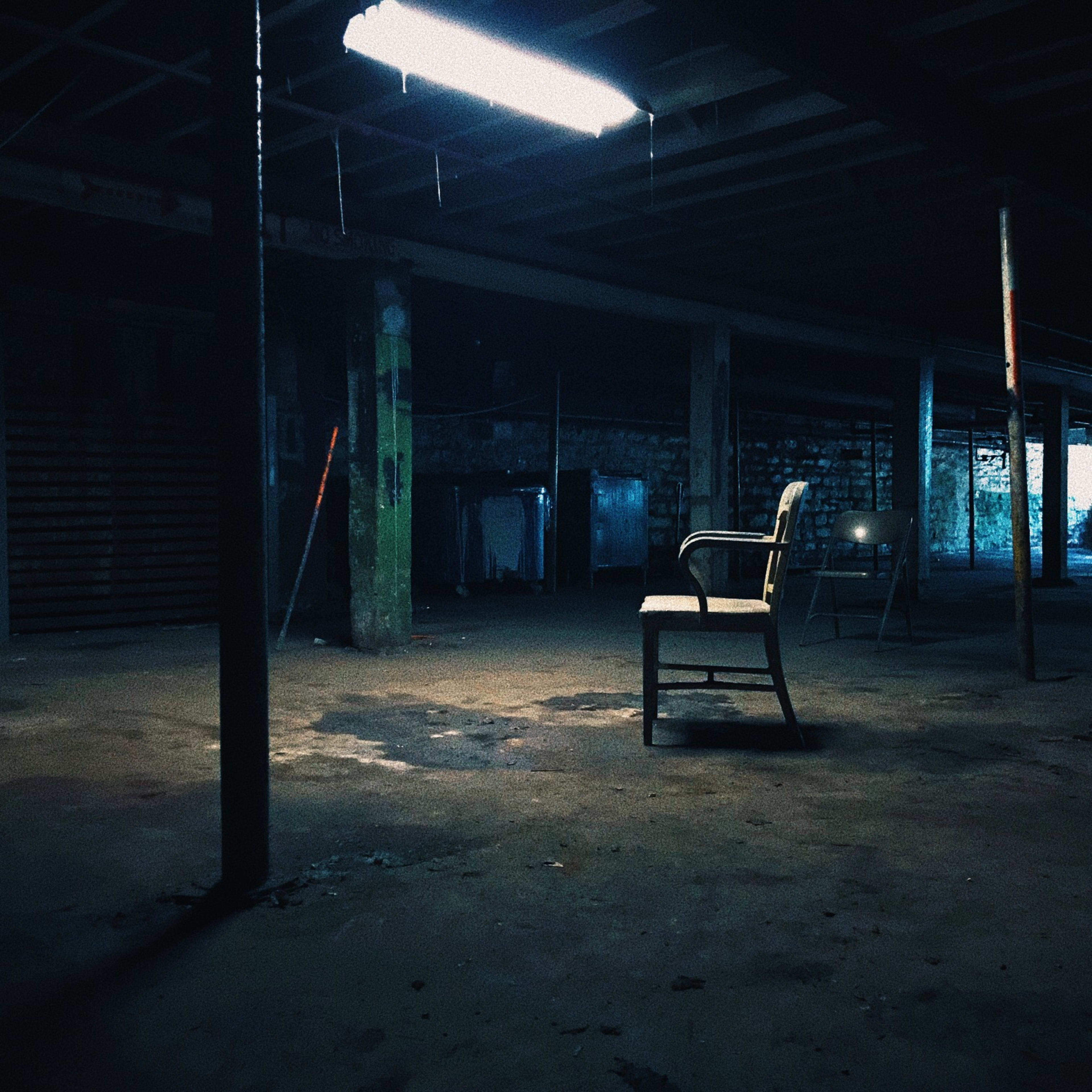 A solitary chair sits on a concrete floor in a dimly lit, empty warehouse space.