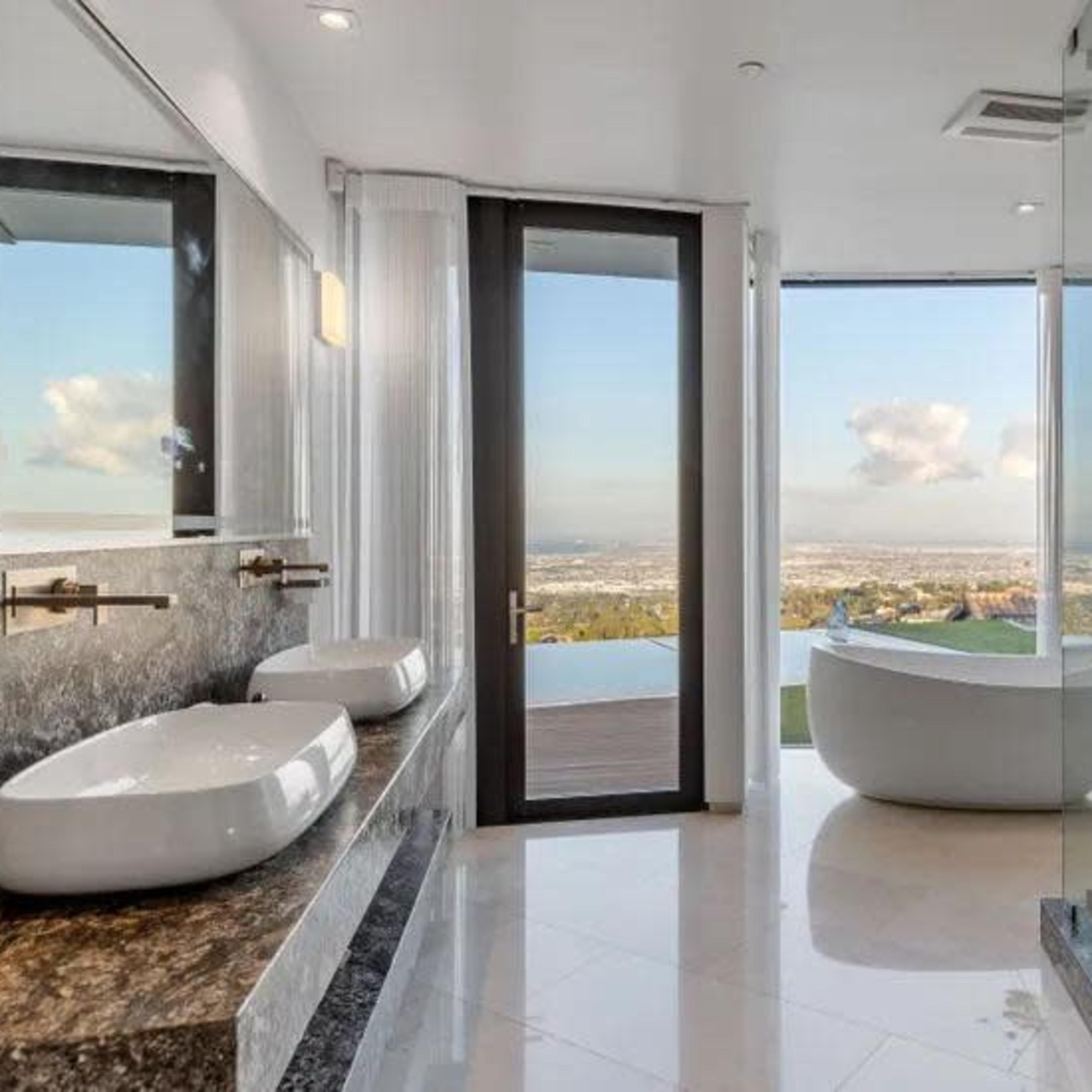 The bathroom features two vessel sinks on a granite countertop, a freestanding bathtub, and large windows offering a panoramic view.