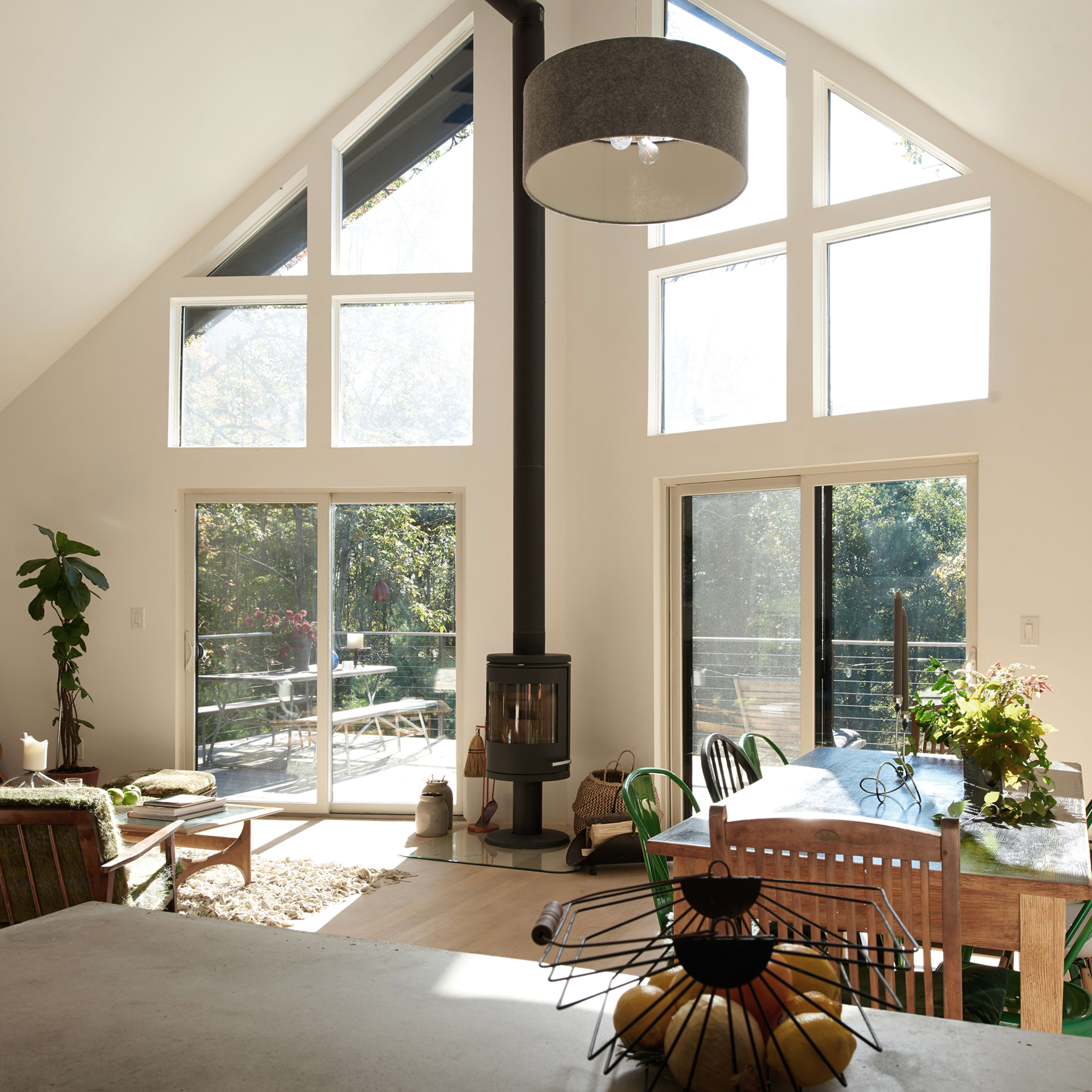 The interior of a modern, sunlit living space features a dining area with a table surrounded by colorful chairs and large windows that overlook a deck.