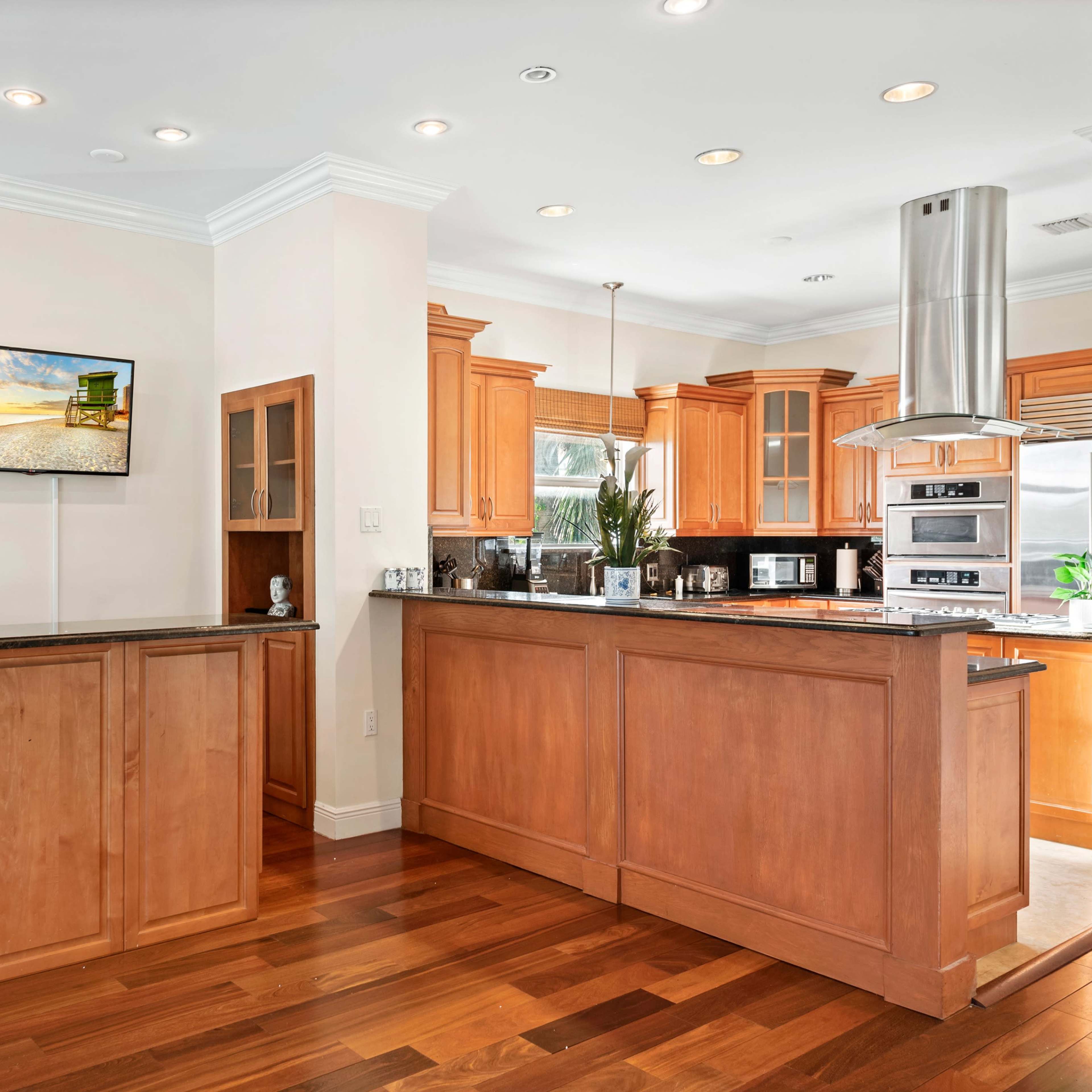 A modern kitchen with wooden cabinetry, stainless steel appliances, and a counter area that includes a television and decorative items.