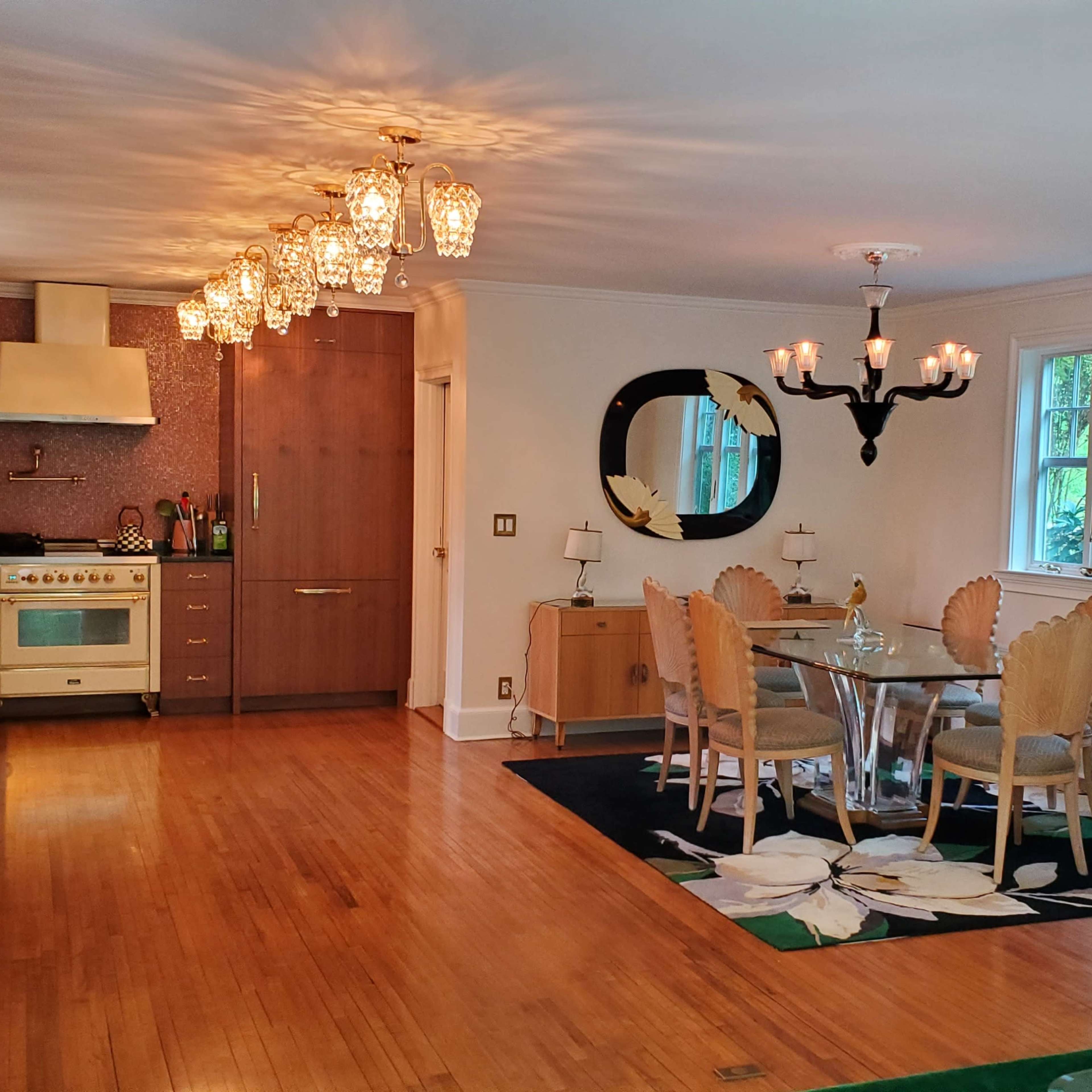 A spacious kitchen and dining area features elegant lighting, a modern chandelier, and a mix of wood and glass furniture.
