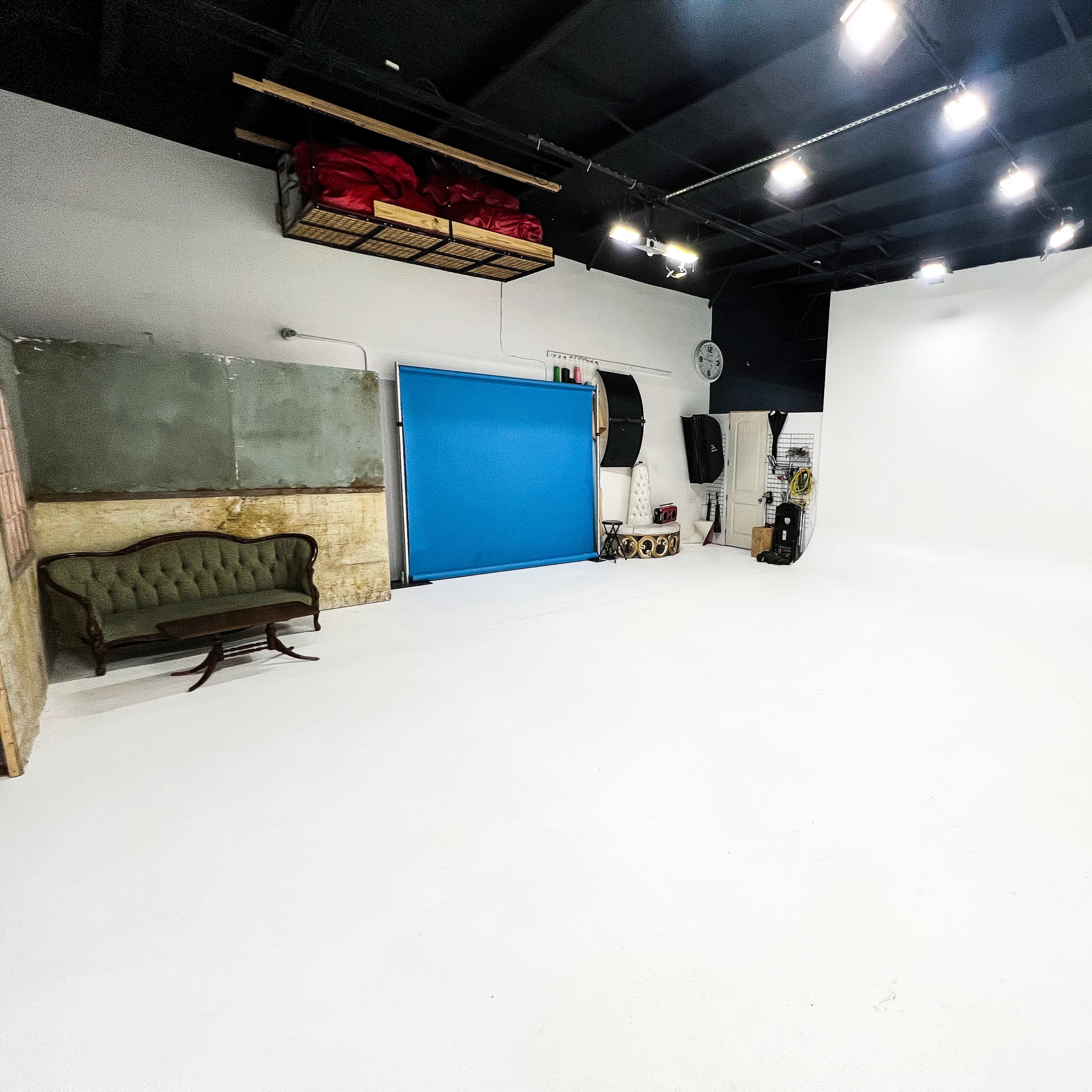 A spacious, empty studio with white walls, a blue rolling door, and a vintage green couch in one corner.