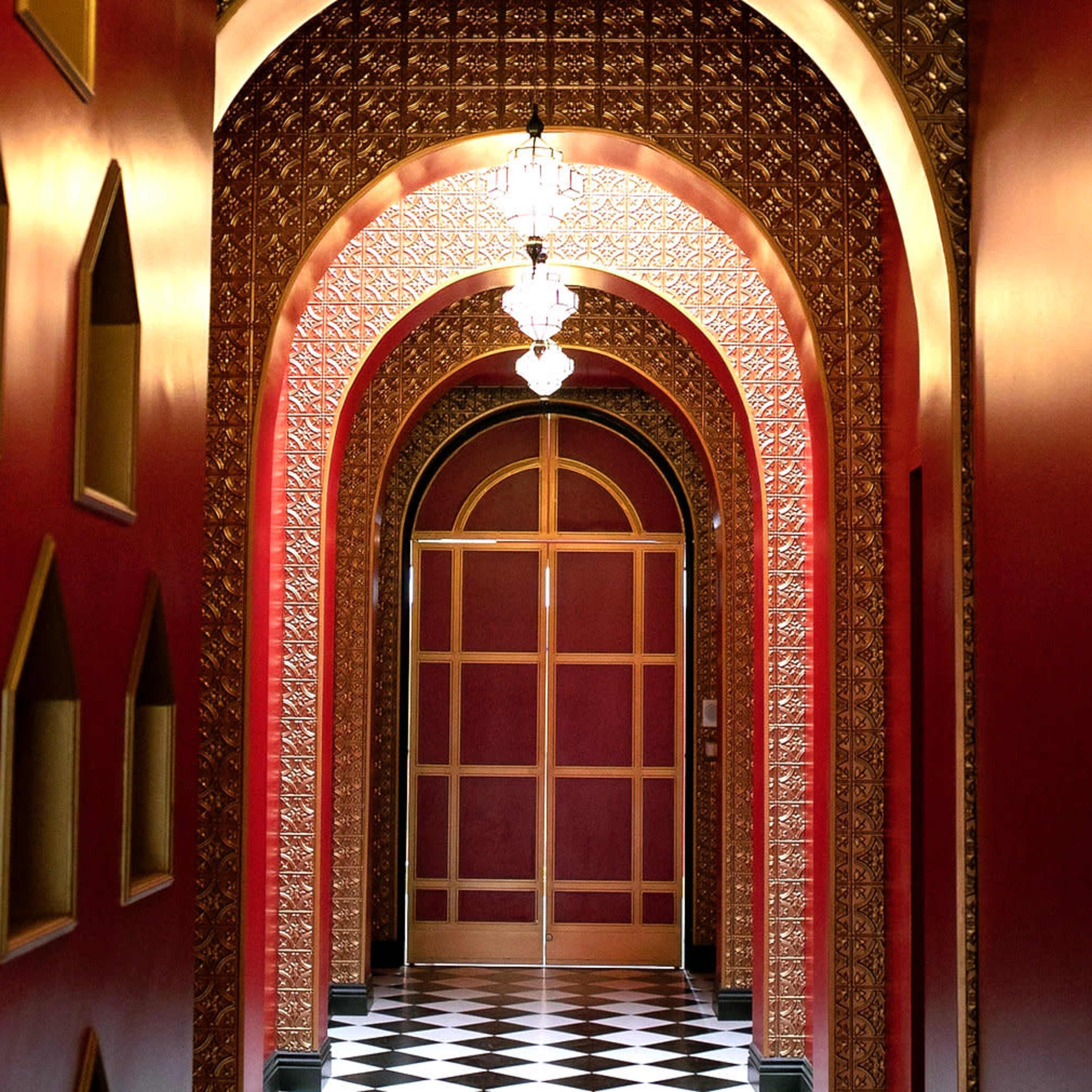 A long corridor features ornate arches and red walls, leading to a wooden door at the end.