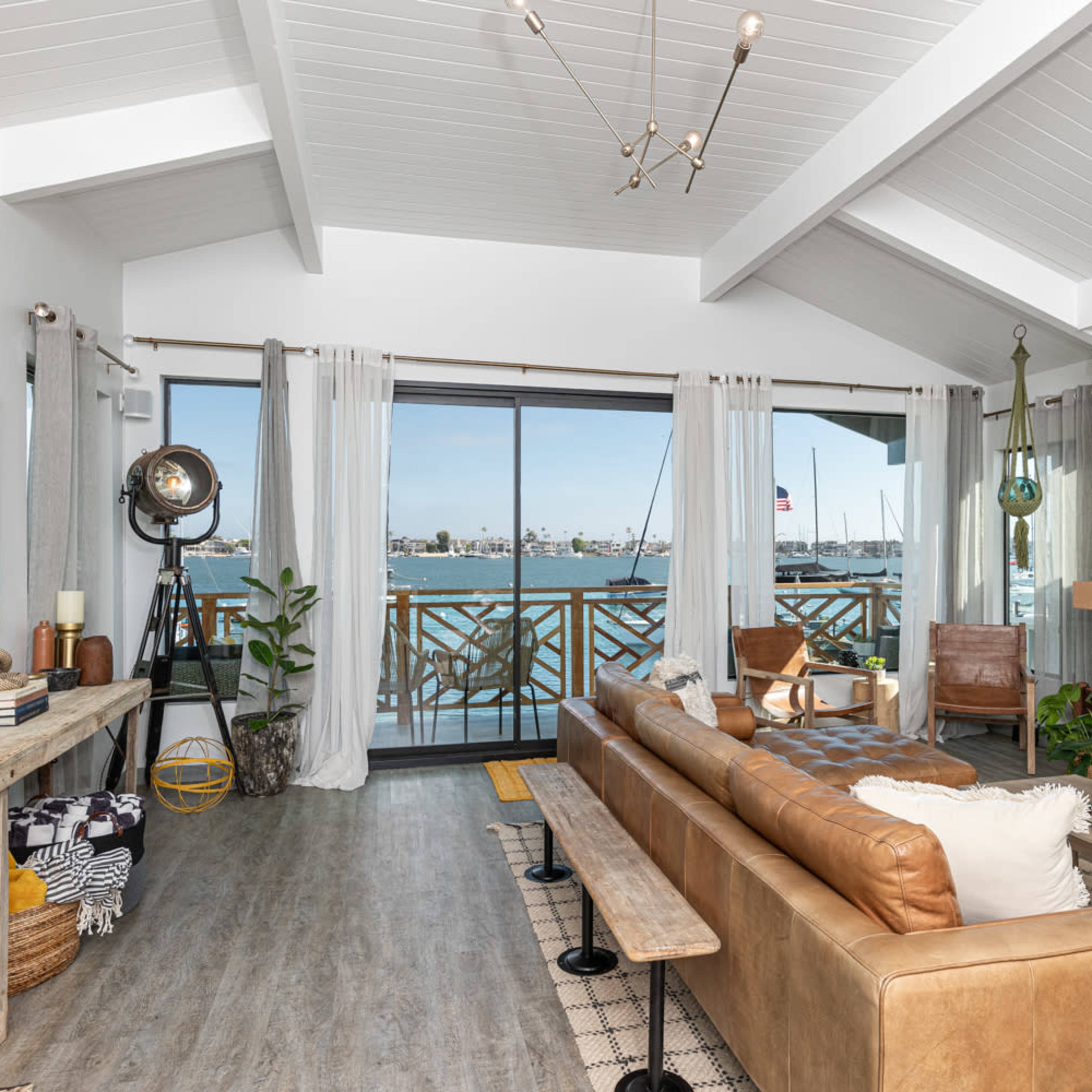A modern living room featuring a leather sofa, a wooden coffee table, and large windows overlooking a waterfront with boats.
