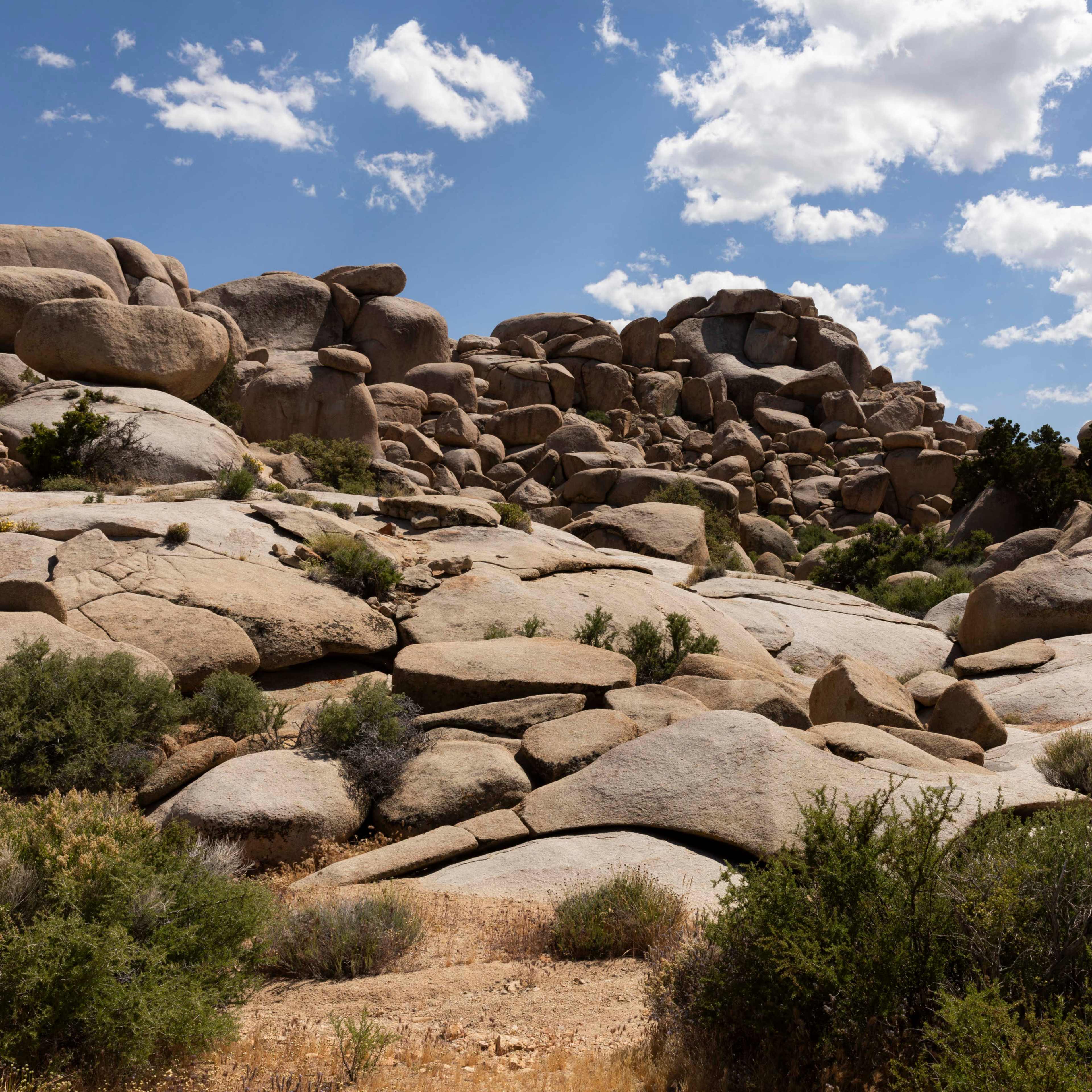 A rocky landscape features large boulders and sparse vegetation under a partly cloudy sky.