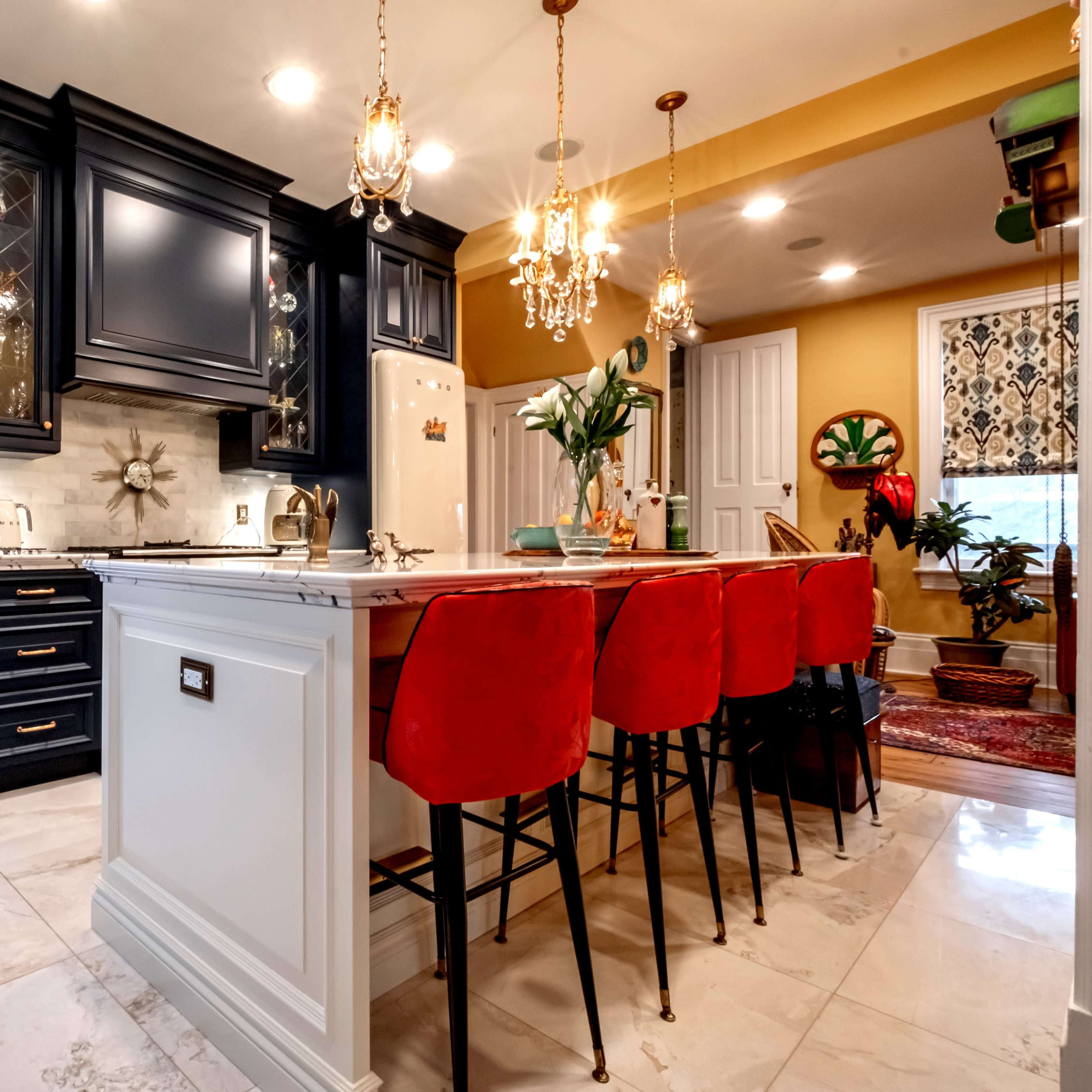 A modern kitchen with a large island featuring red bar stools, black cabinetry, and pendant lights.