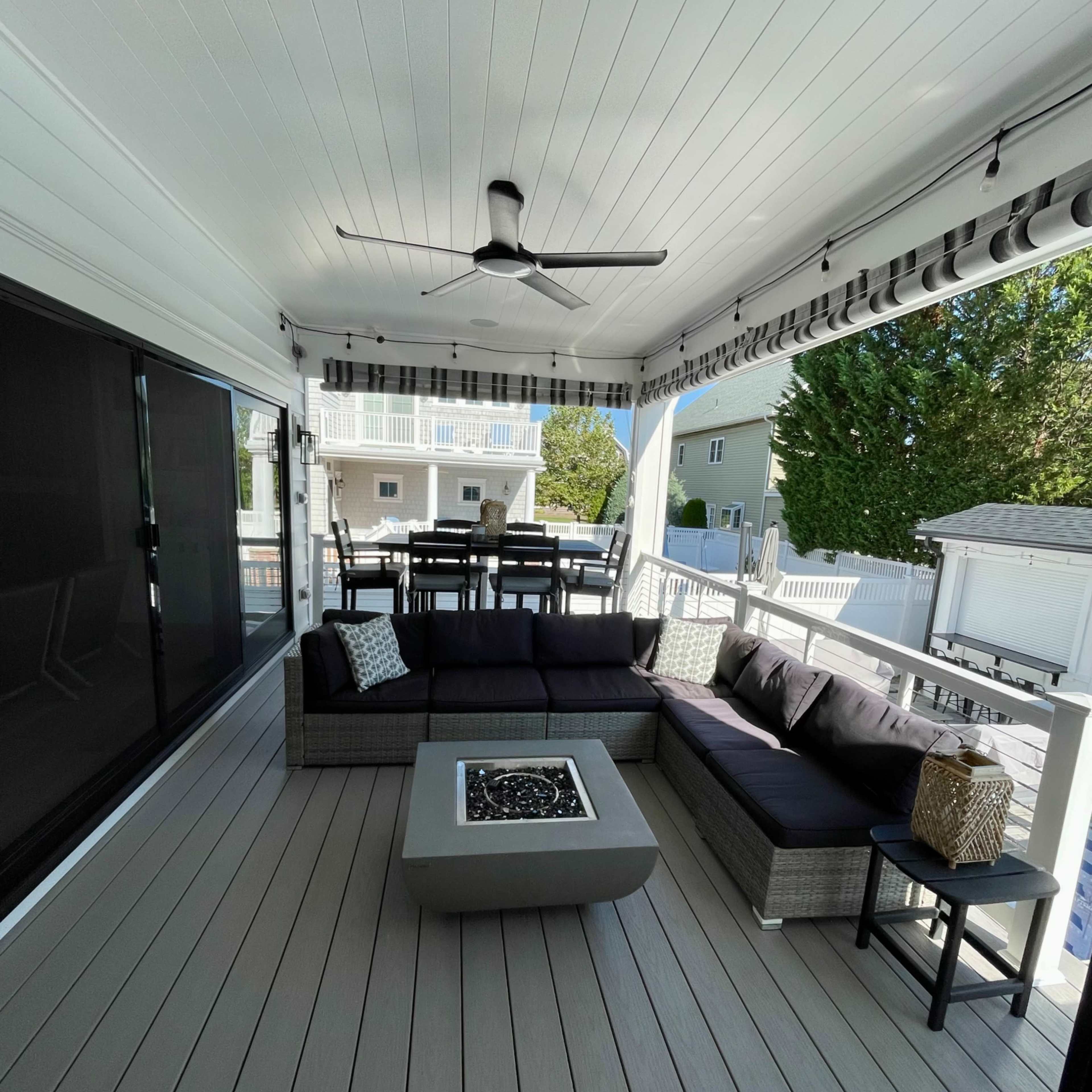 A covered outdoor patio featuring a sectional sofa, a fire pit table, and a dining area set with chairs.