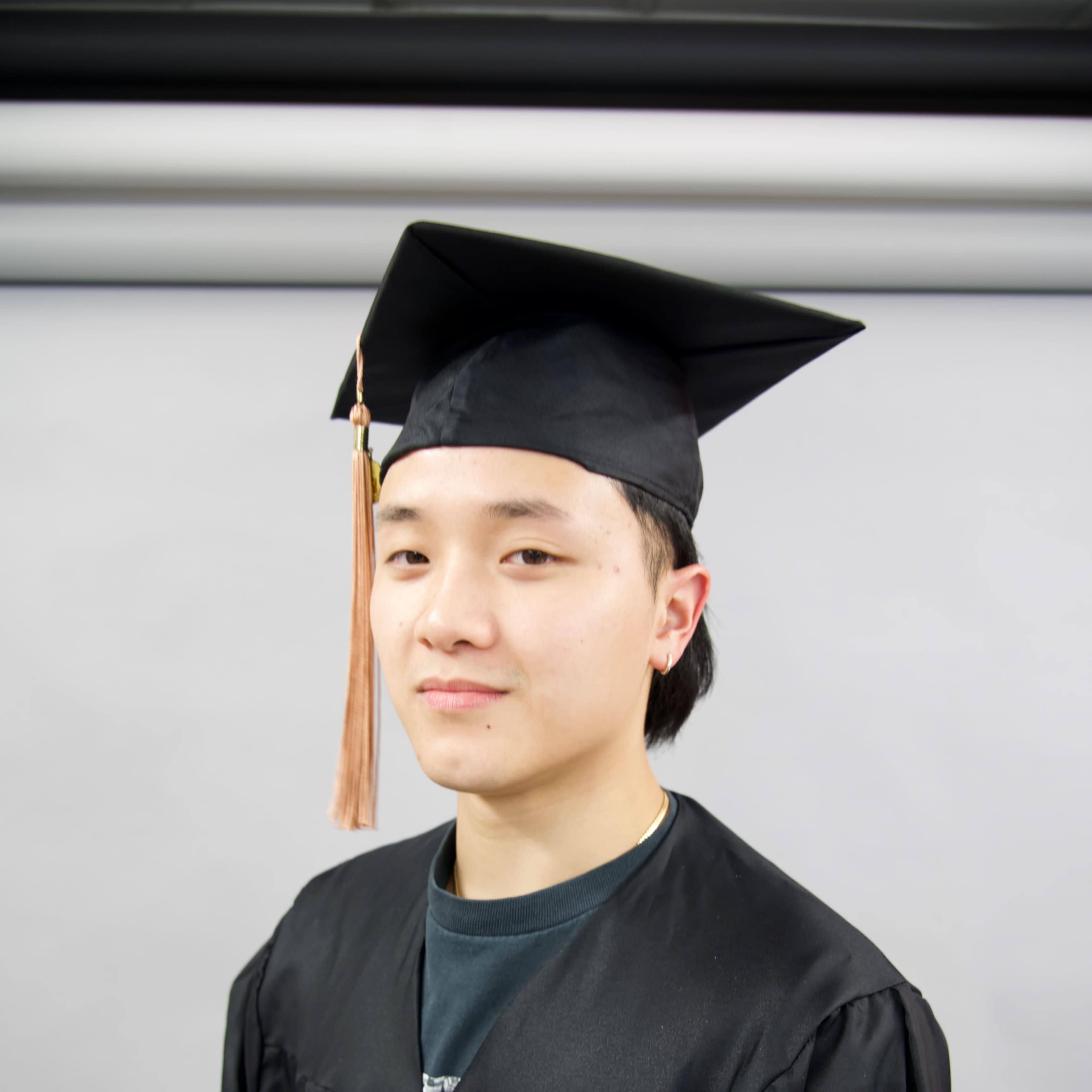 A young man wearing a graduation cap and gown poses for a portrait.