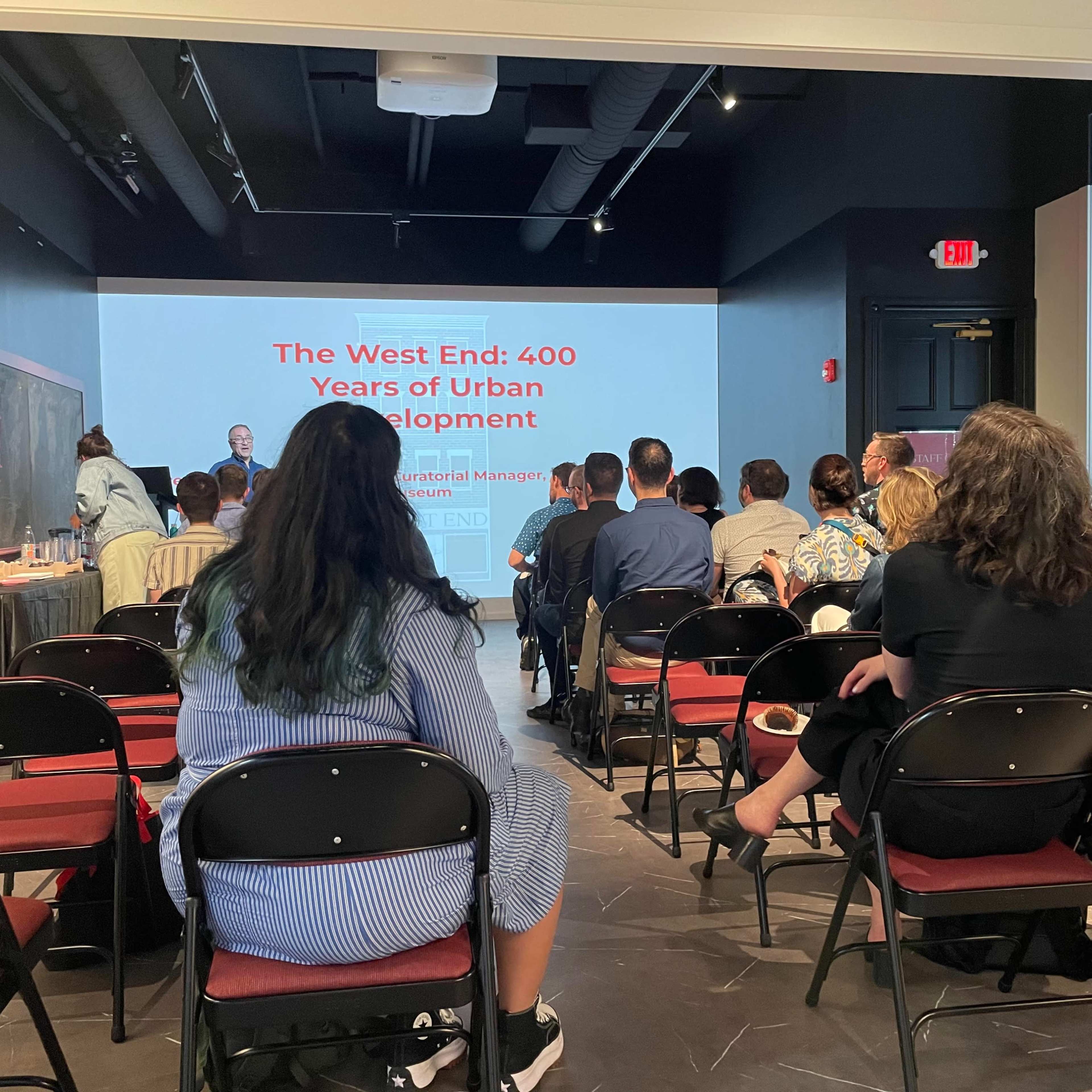 A group of attendees is sitting in a meeting room while listening to a presentation titled "The West End: 400 Years of Urban Development."
