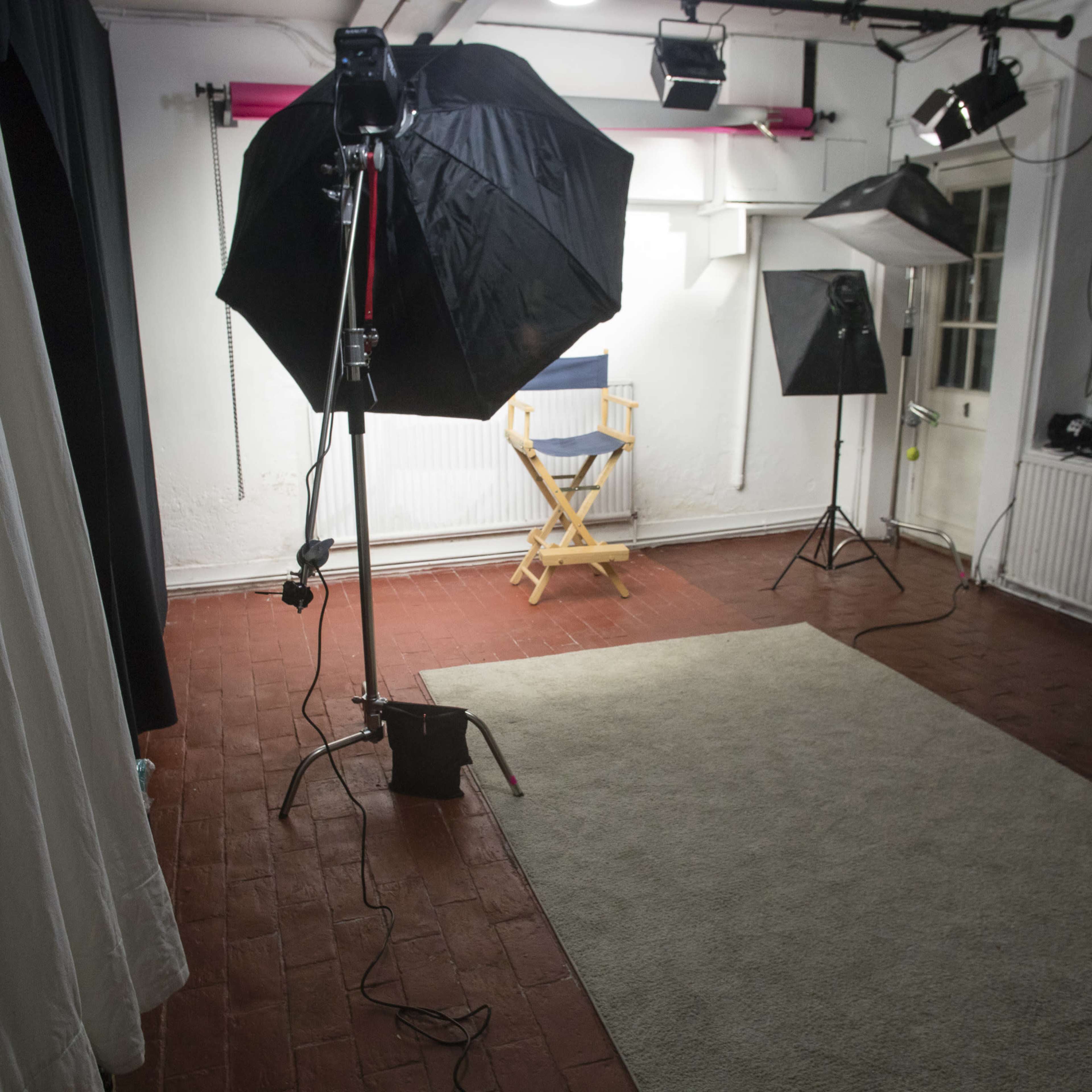 A photography studio setup with various lighting equipment, a director's chair, and a rug on the floor.