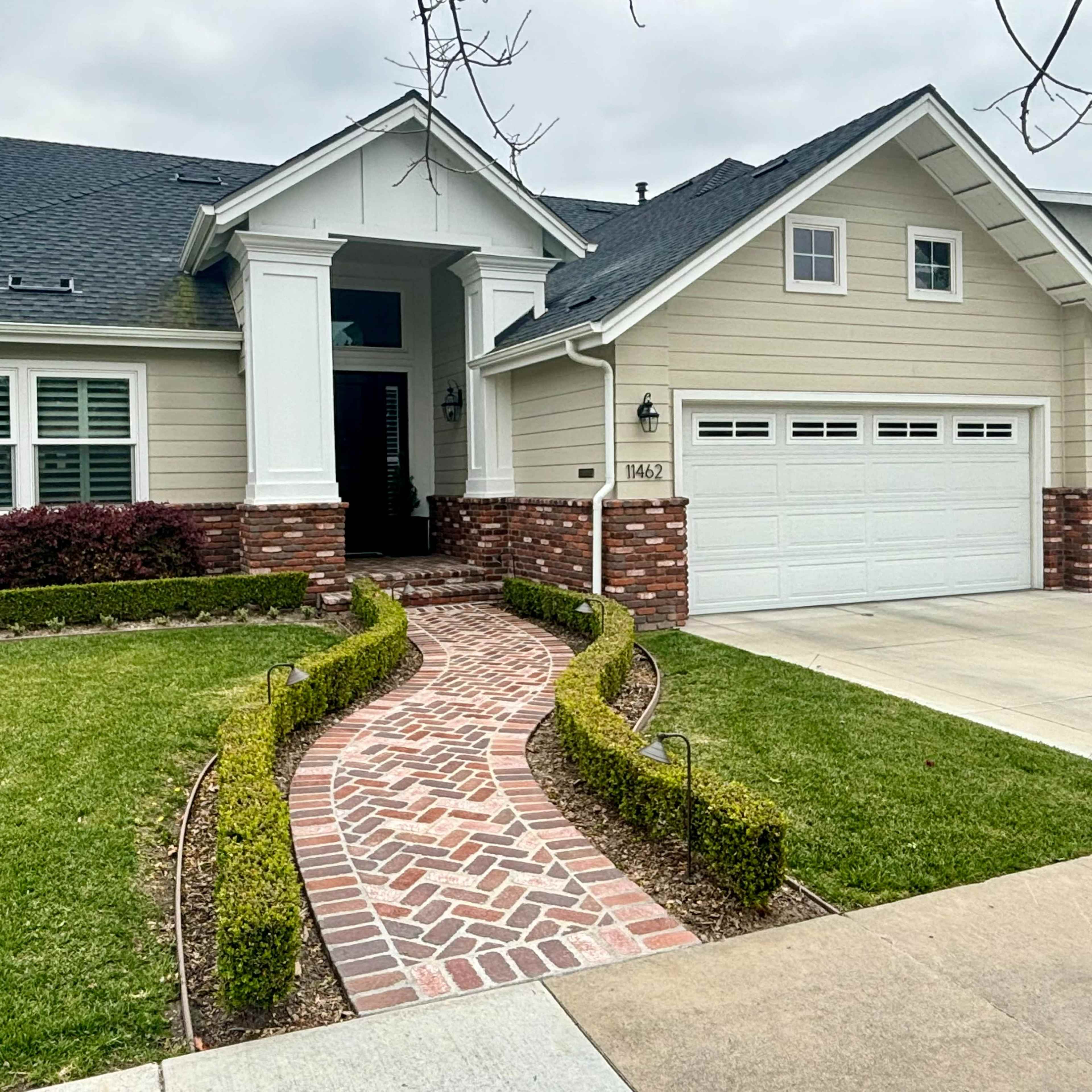 A single-story house with a light-colored exterior and brick accents, featuring a curved brick walkway leading to the front door.
