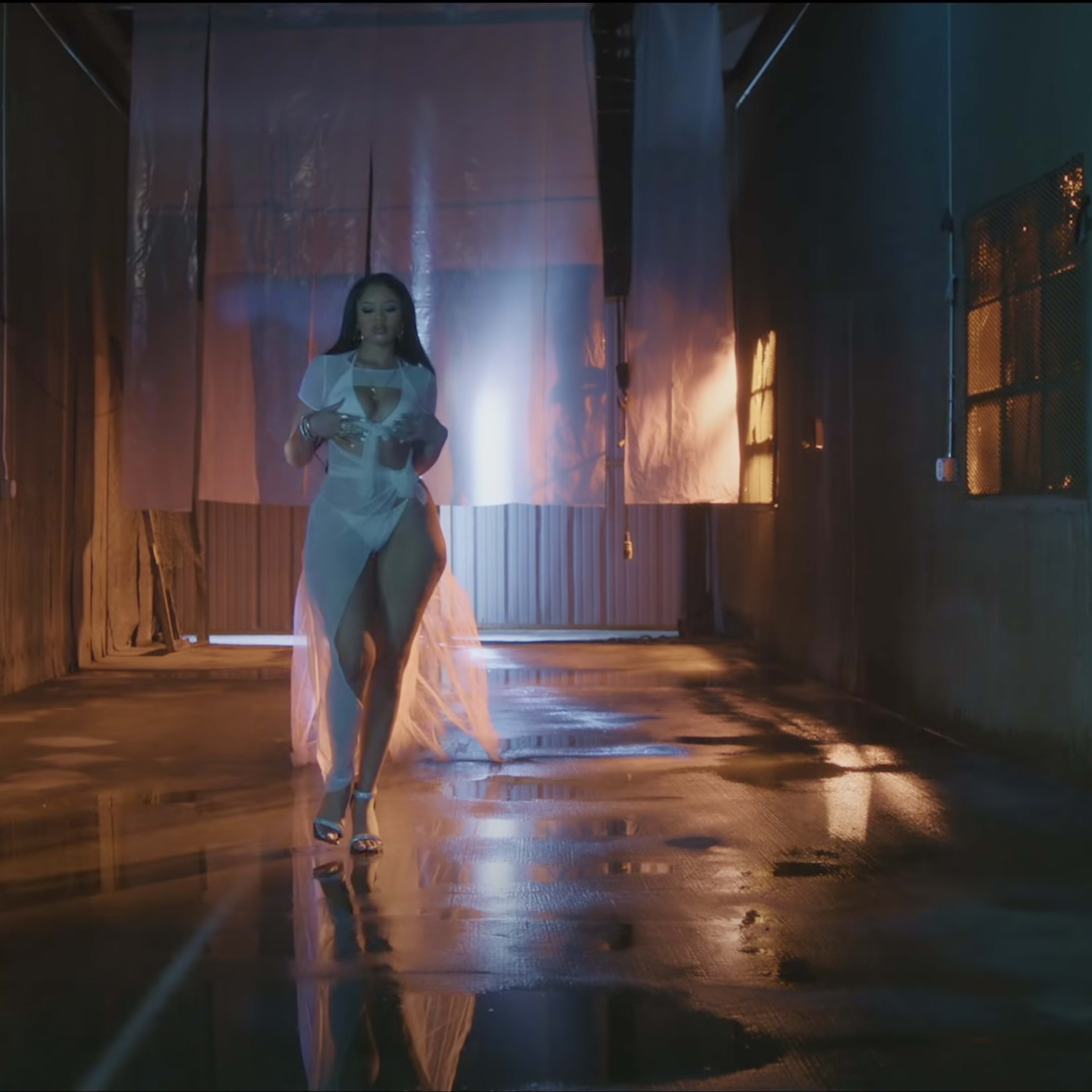 A woman walks through a narrow, dimly lit corridor with reflective wet floors and industrial walls.