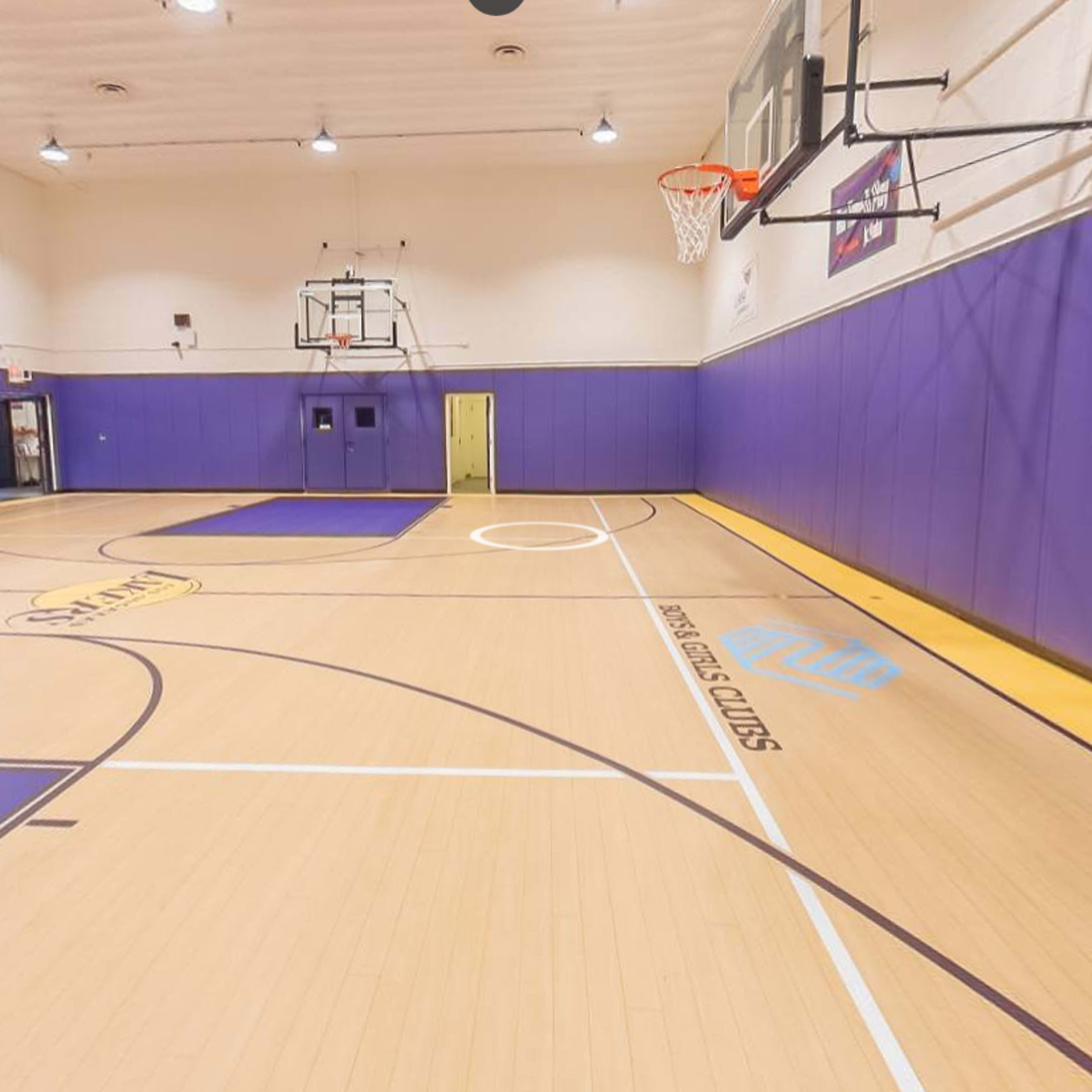A basketball court with purple walls, two basketball hoops, and a smooth wooden floor marked with court lines.