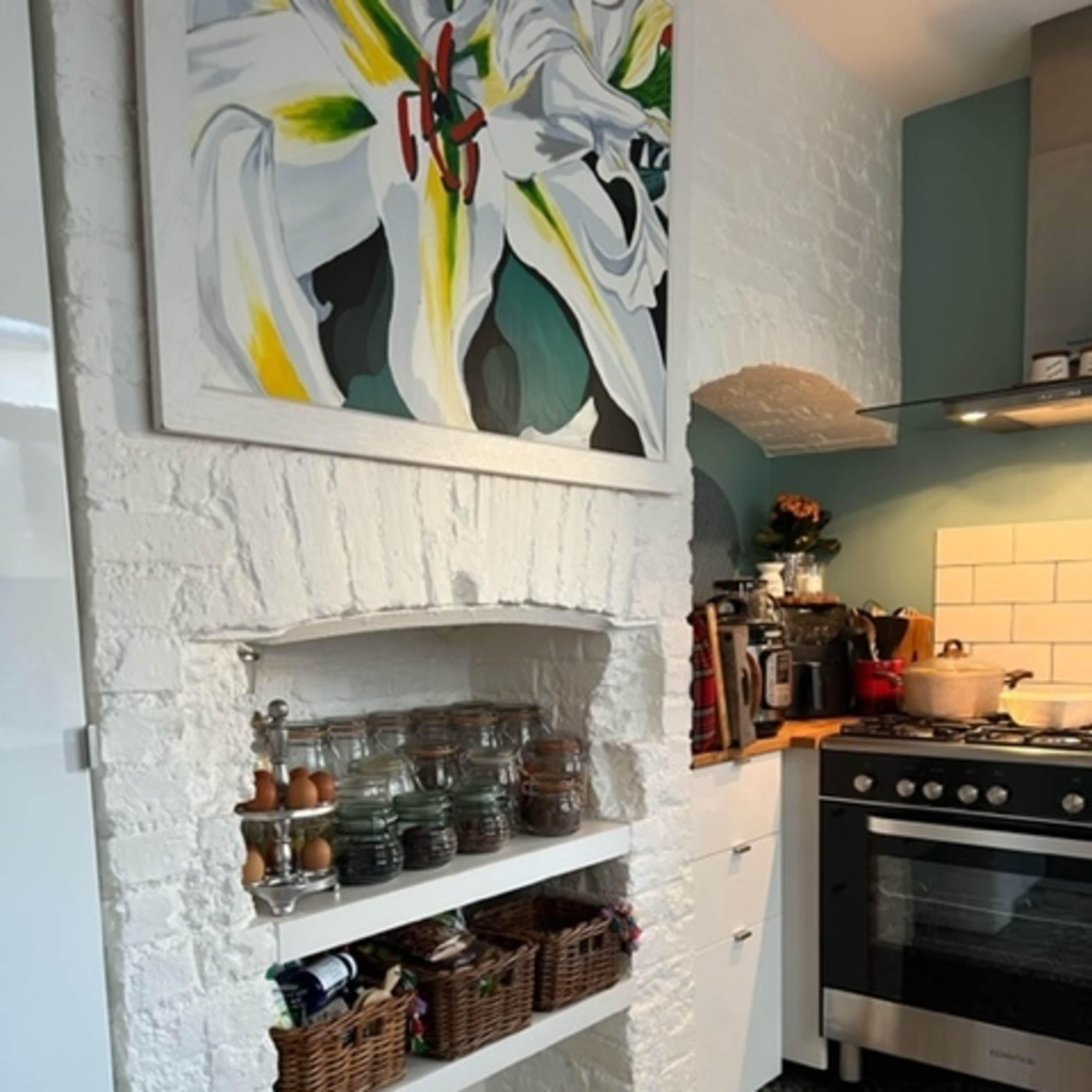 A kitchen with a white brick archway housing glass jars and baskets, a gas stove, and a colorful painting on the wall.