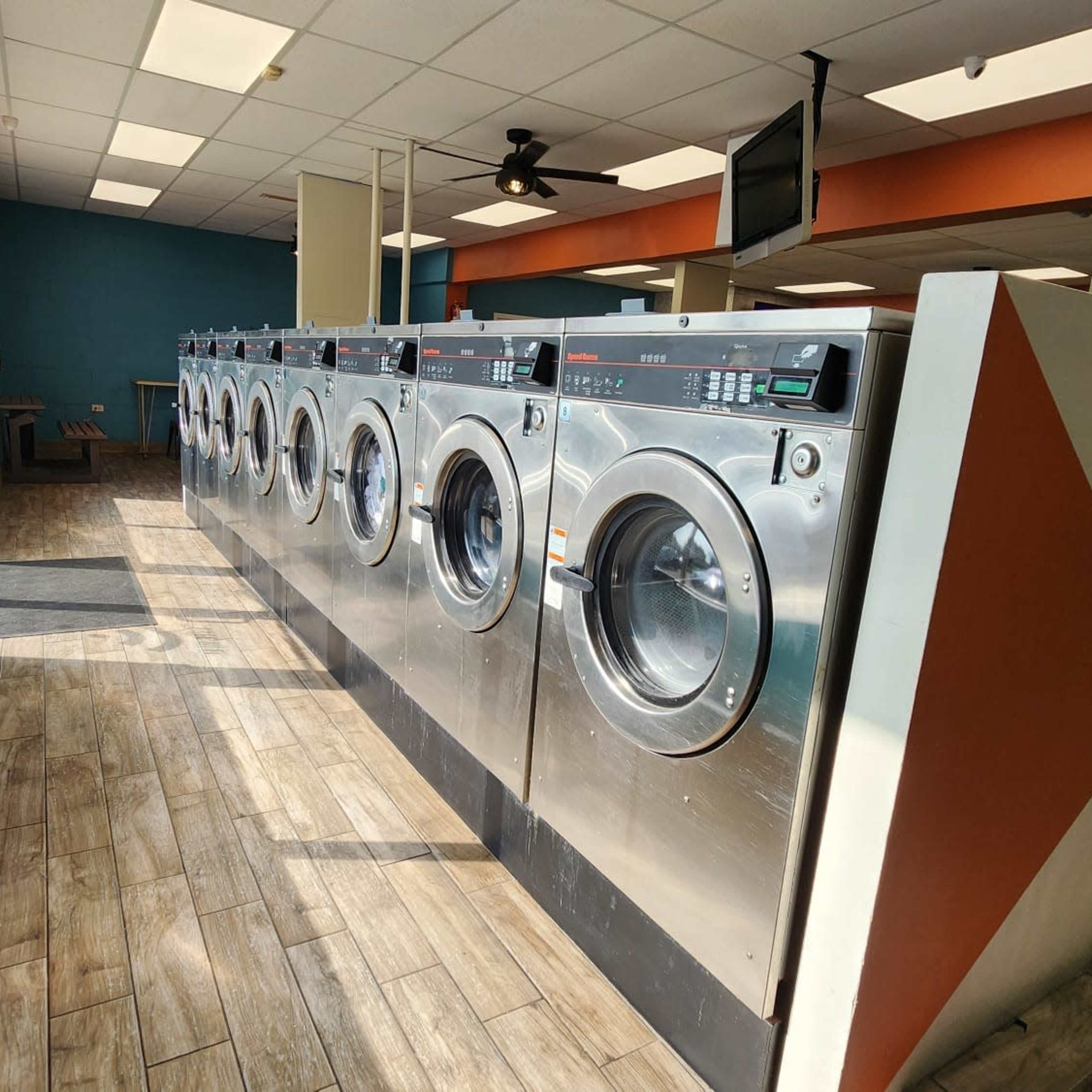 A row of commercial washing machines in a brightly lit laundromat with a blue and orange color scheme.