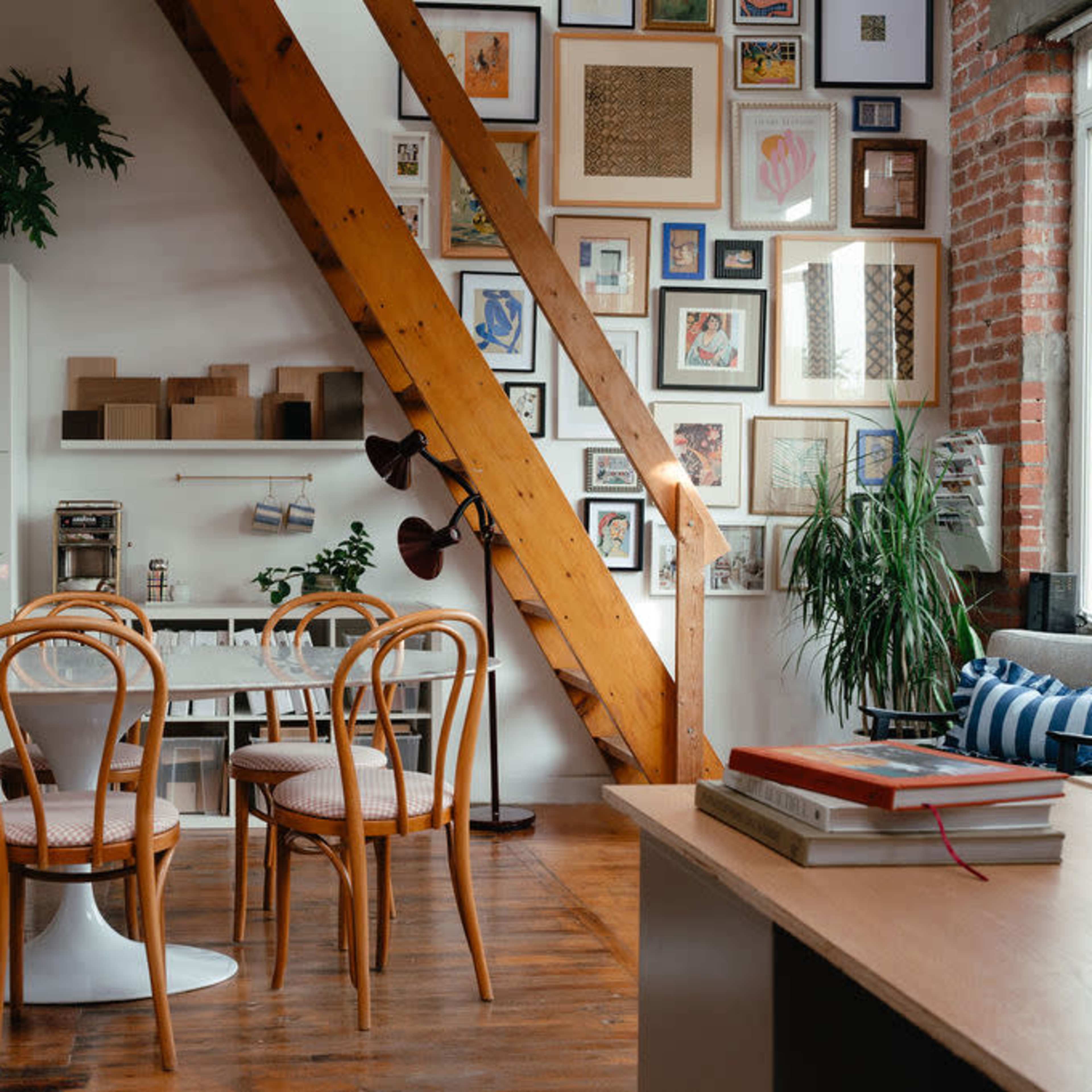A dining area features a round table surrounded by wooden chairs, with a background of a gallery wall and exposed wooden beams.