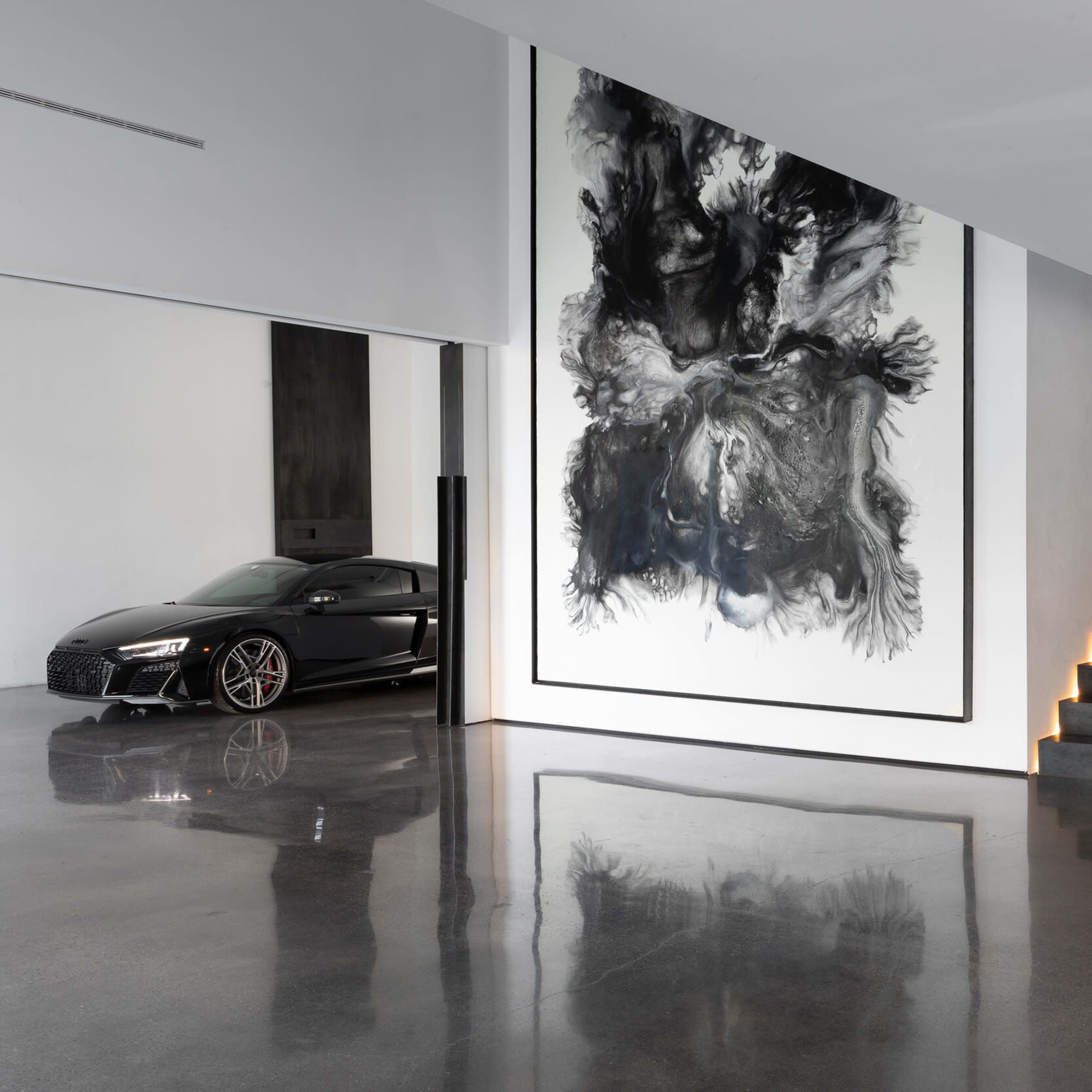 A modern interior features a sleek black car parked beside a large abstract artwork and a bronze sculpture, with a staircase leading to an upper level.