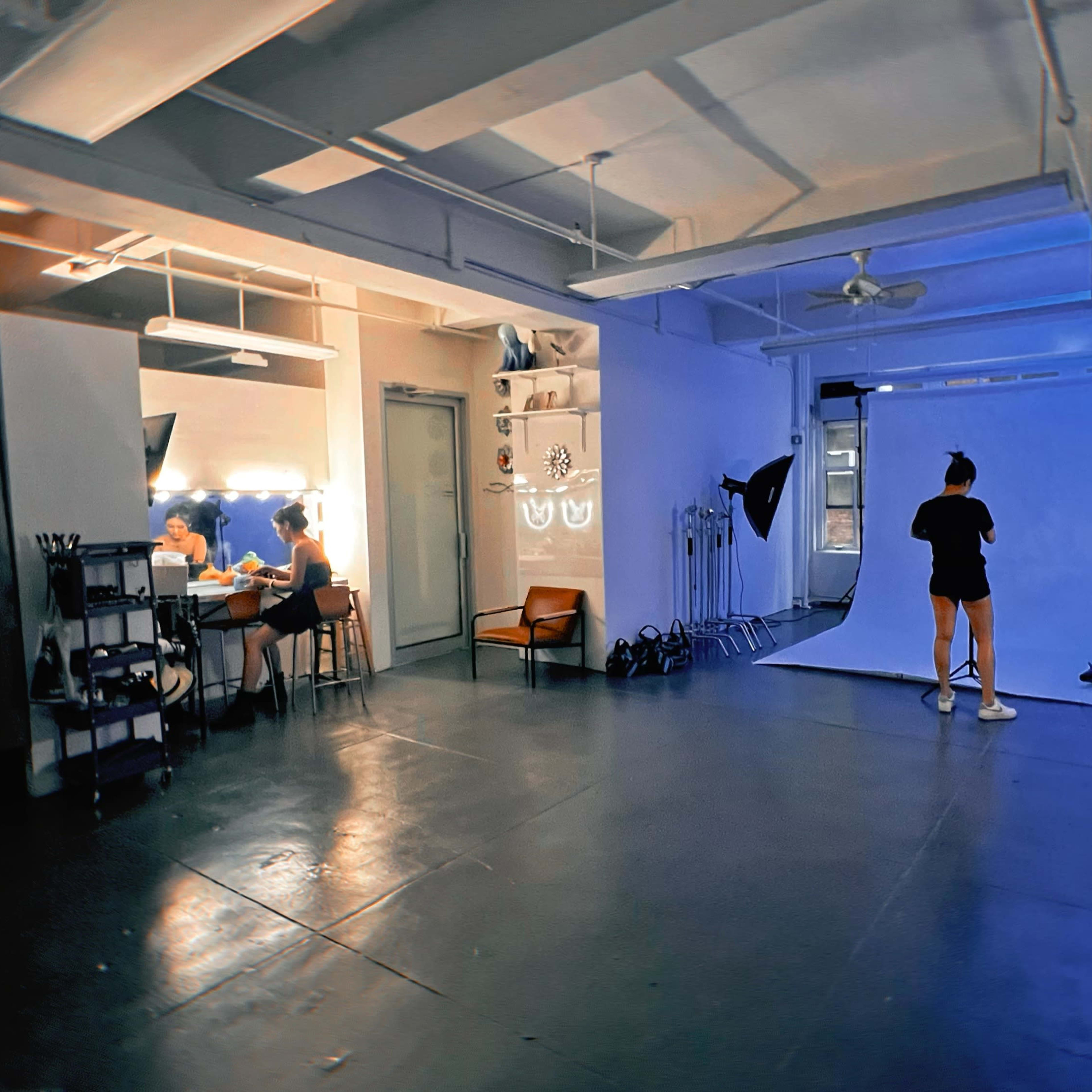 A spacious studio with a blue backdrop, equipped with lighting equipment, and a table where two people are seated.