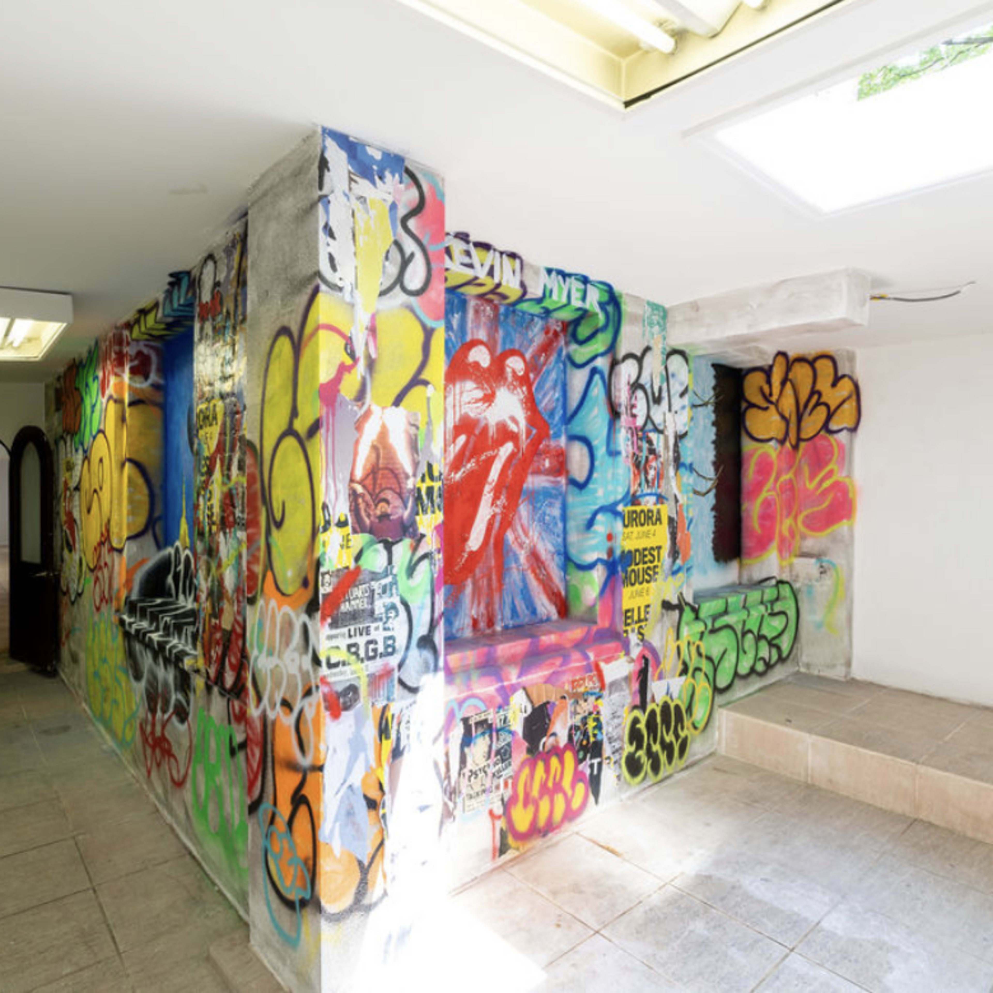 A hallway with walls covered in vibrant graffiti and street art, contrasting with the plain tiled floor and ceiling.