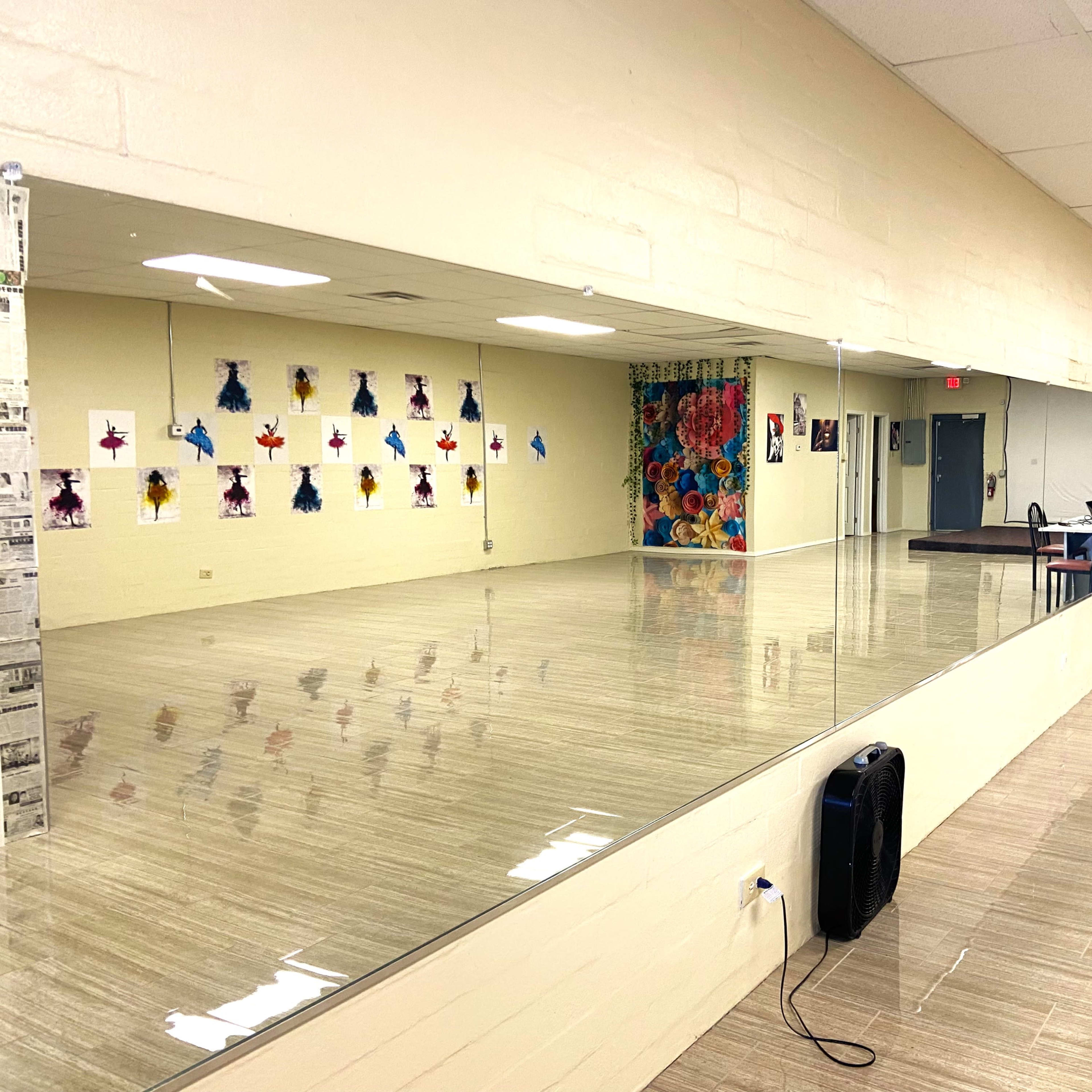 A large dance studio features a mirrored wall, colorful wall decorations, and a seating area with tables and chairs.