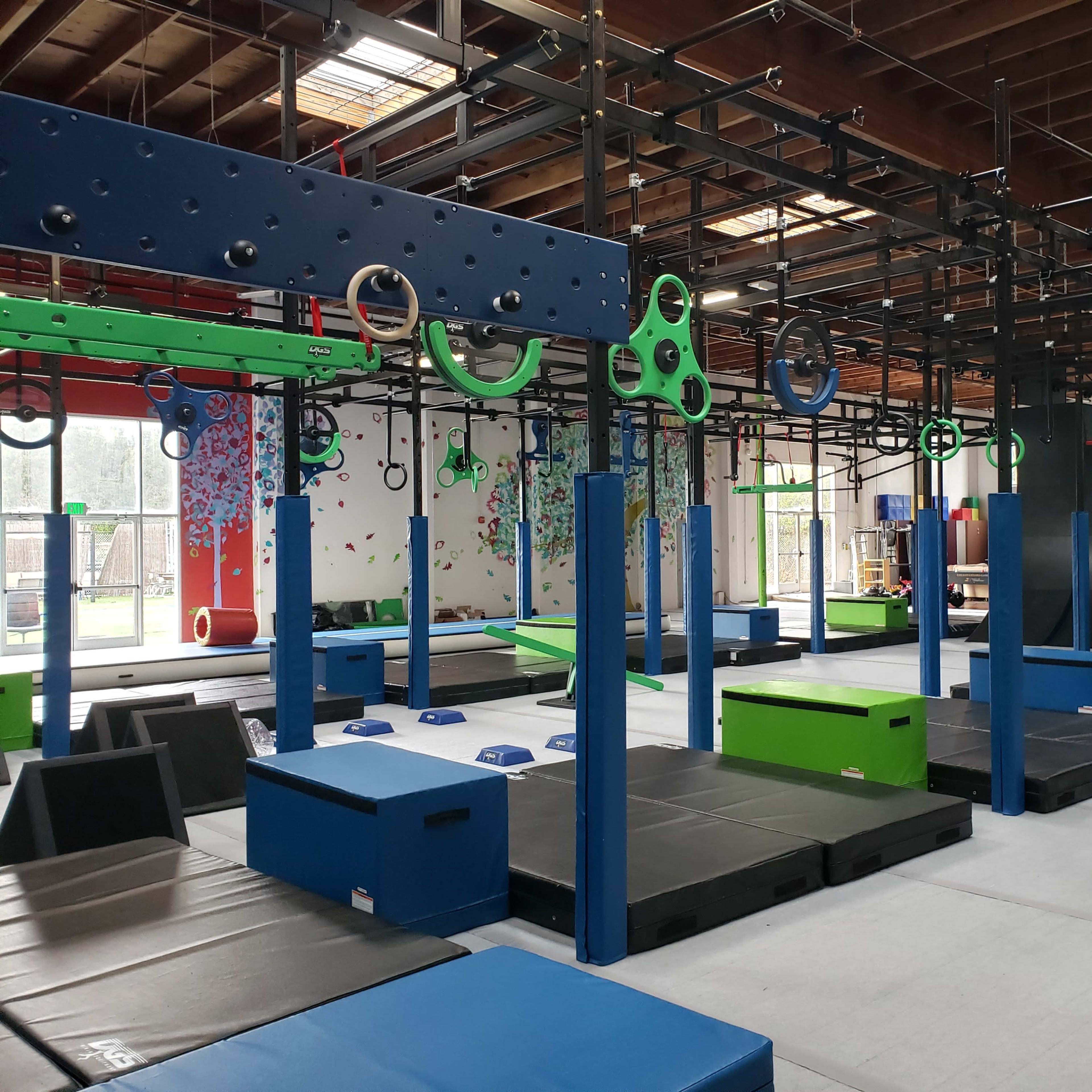 An indoor gym with various training equipment, including climbing structures, mats, and rings, arranged in a spacious facility.