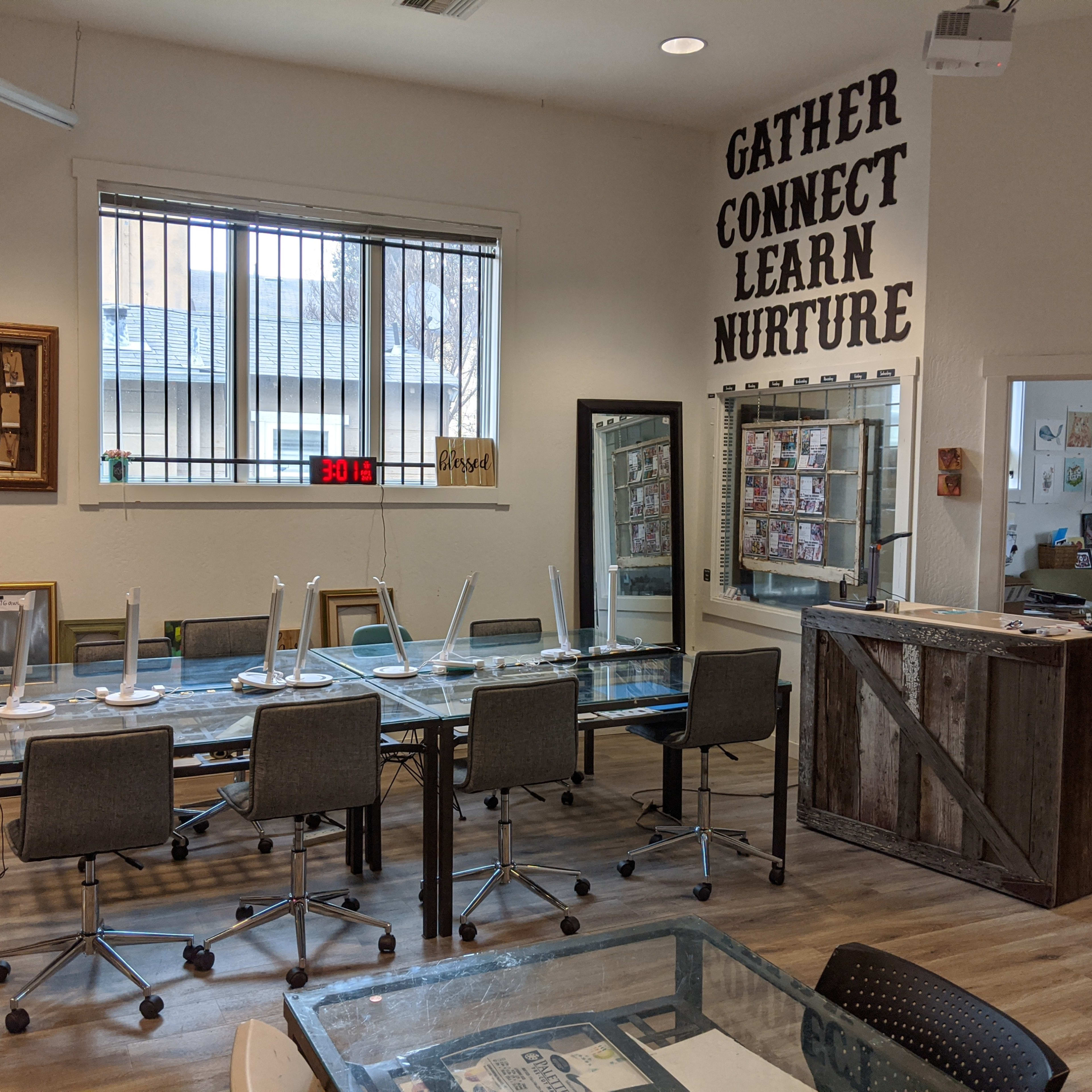 A conference room features a long glass table surrounded by rolling chairs, with inspirational words displayed on the wall and a view of a courtyard through the window.