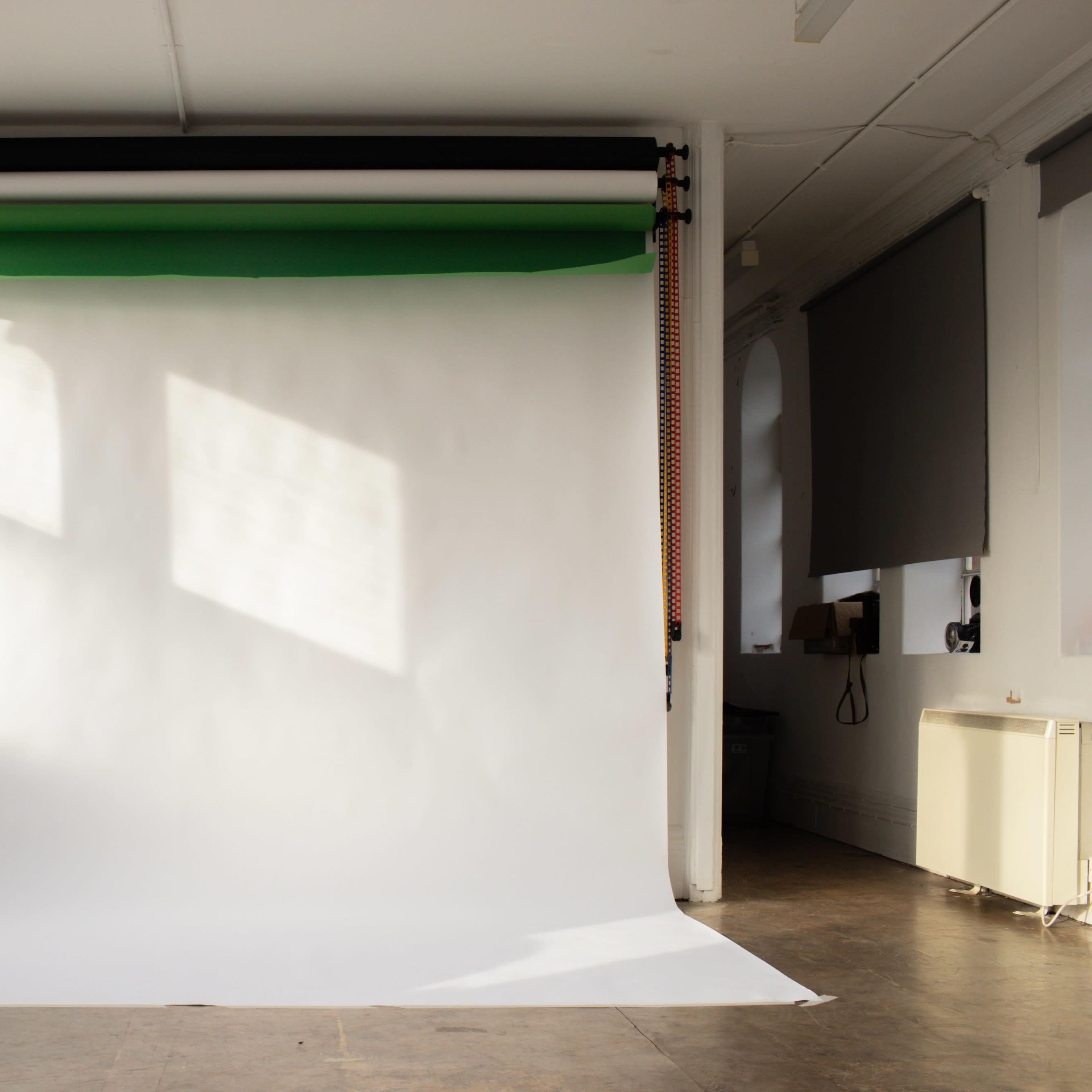 An empty photography studio with a white backdrop and colored paper rolls hanging above.