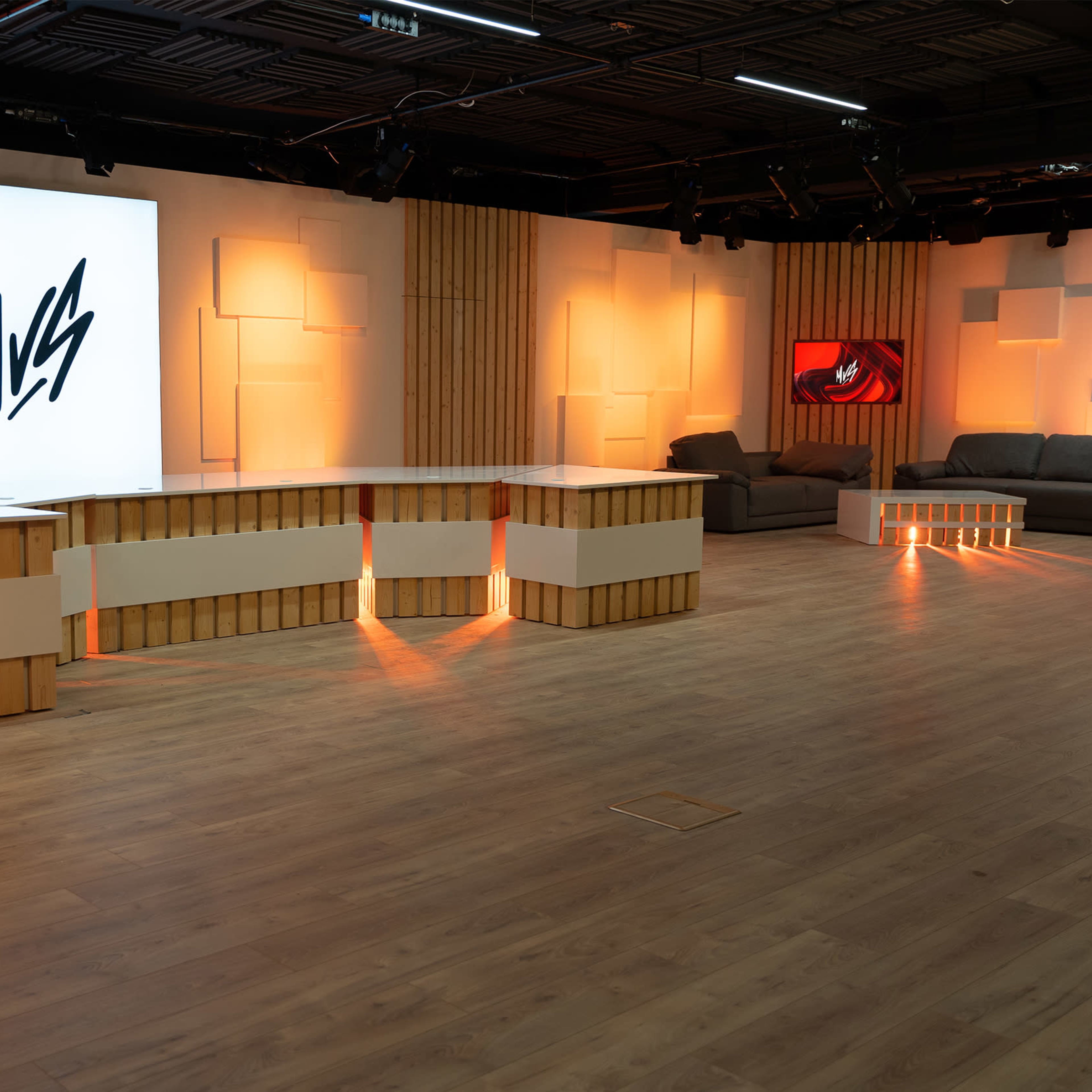 A modern studio space featuring a large logo on a light panel, a sleek reception desk with illuminated accents, and a cozy seating area with a dark sofa.