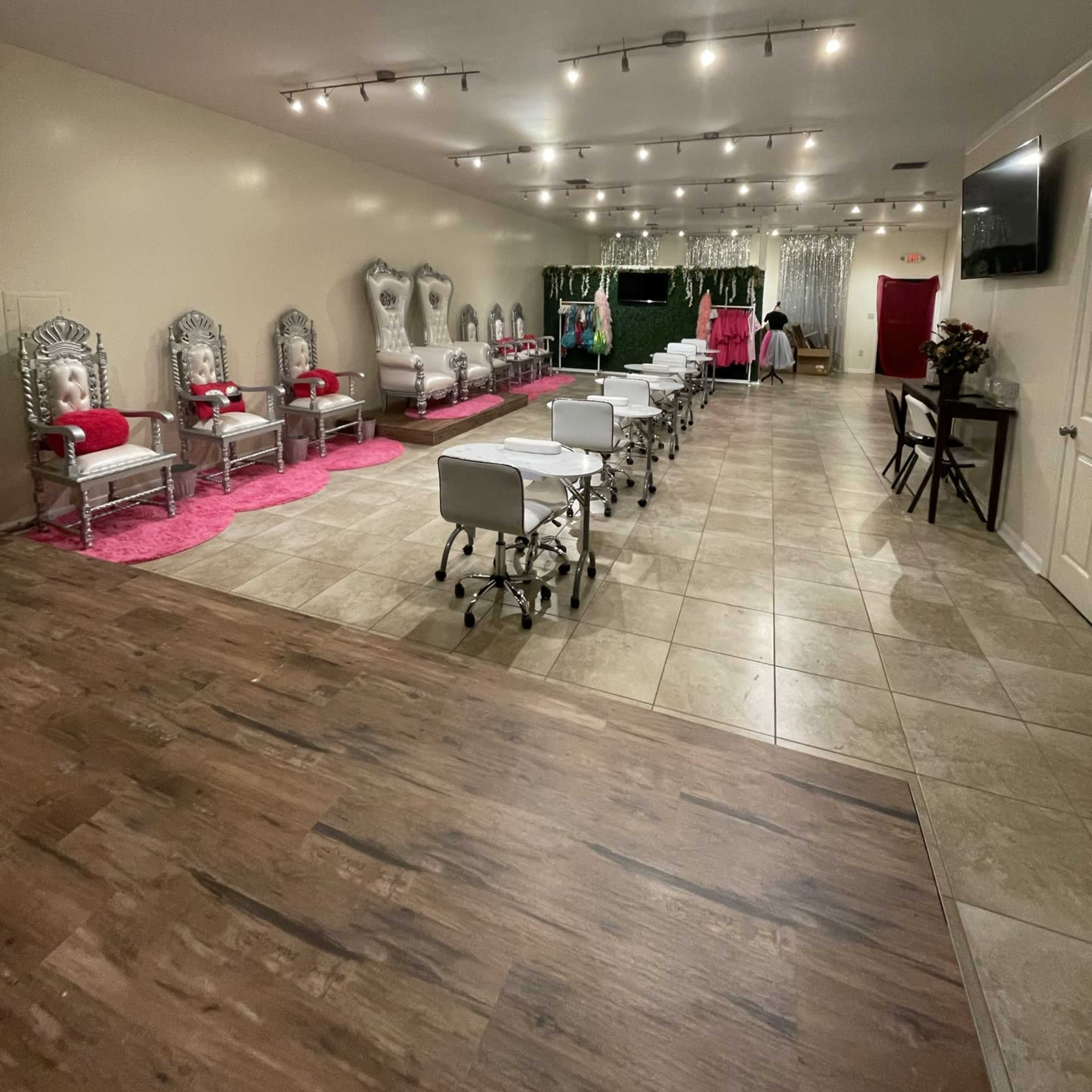A spacious event room with silver chairs, white treatment tables on tiled flooring, and pink accents, including a plush pink carpet.