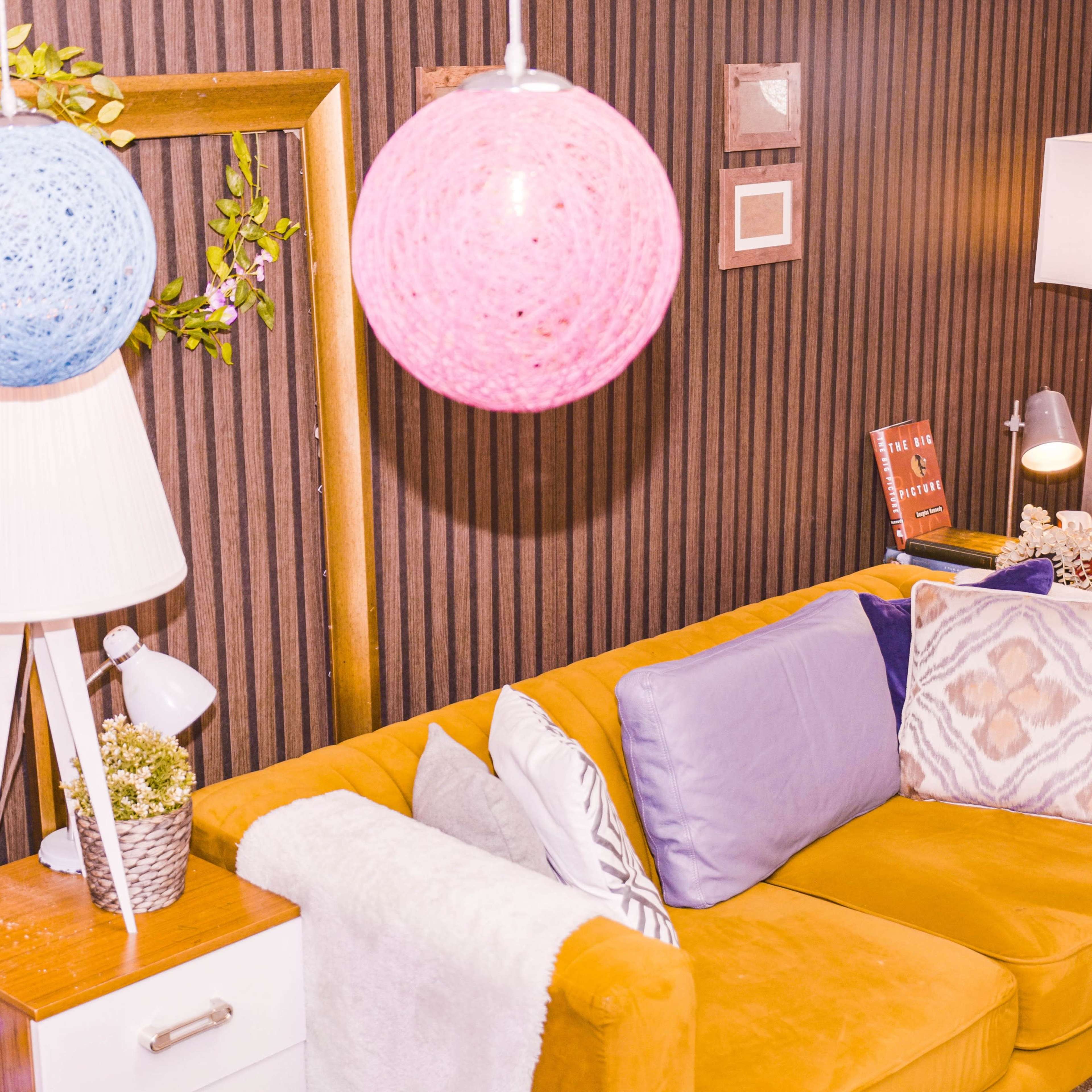 A cozy living room with a yellow sofa, colorful hanging lanterns, and decorative plants against a wooden striped wall.