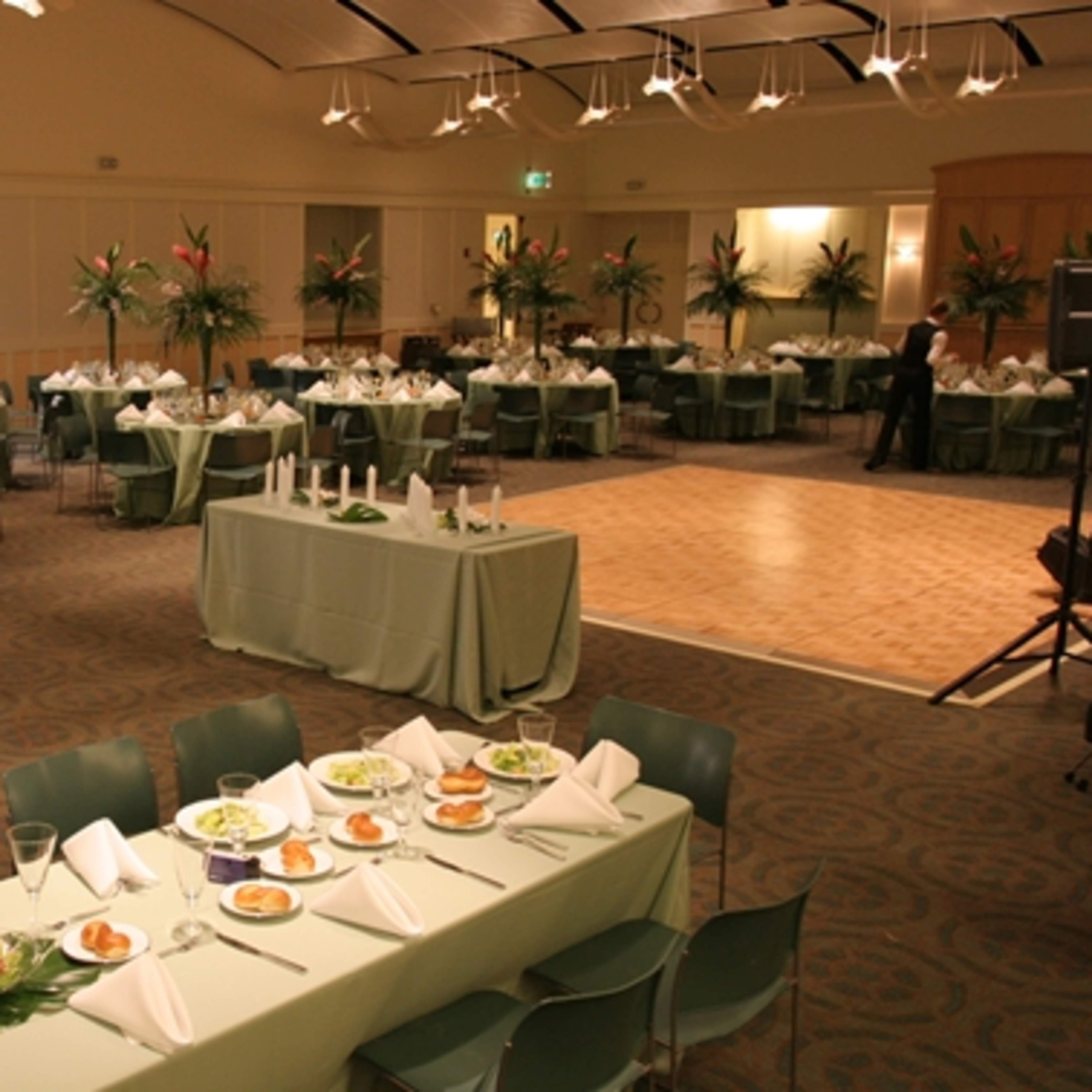 A banquet hall arranged with multiple dining tables set with plates, glassware, and decorative centerpieces.