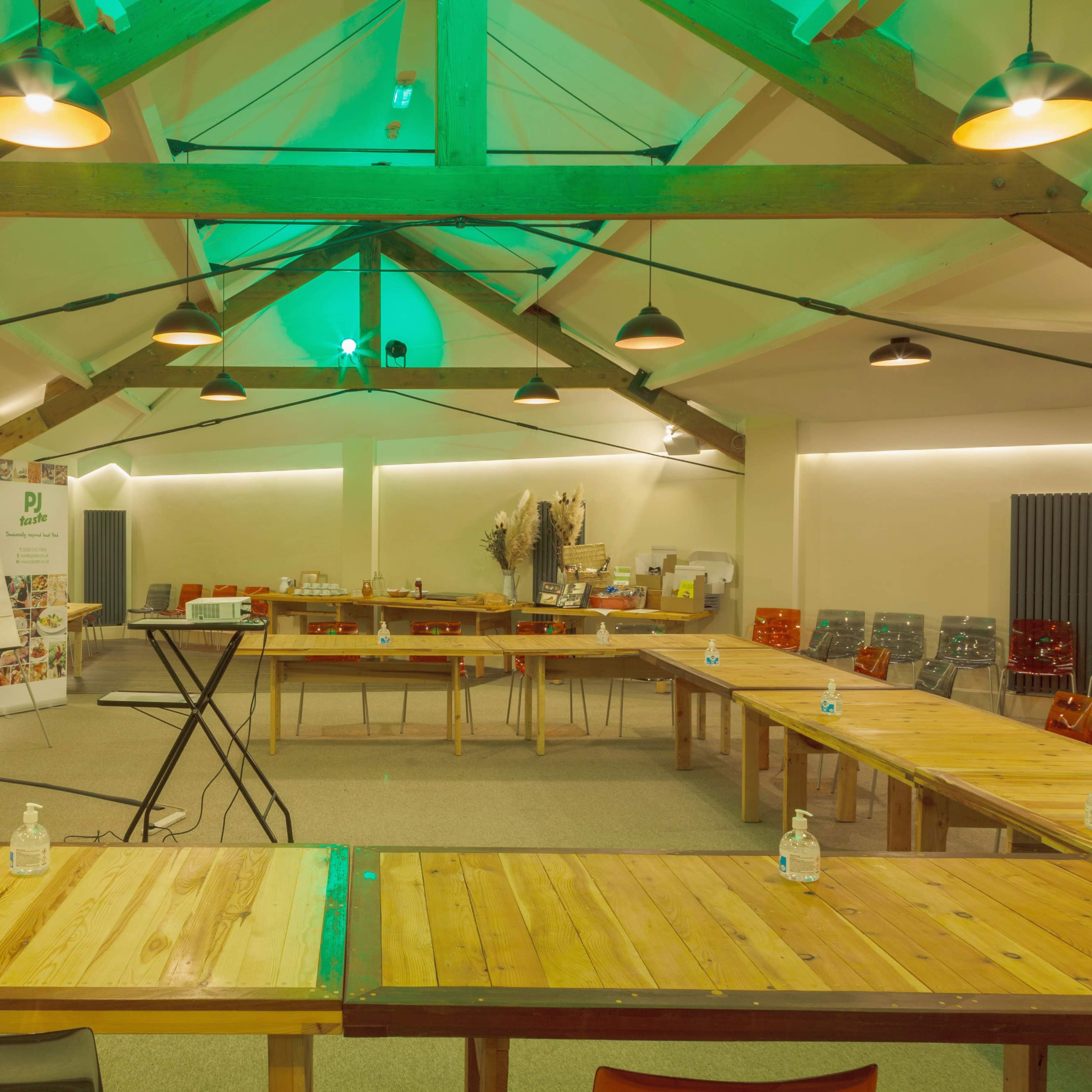 An indoor meeting space with wooden tables arranged in a U-shape, surrounded by colorful chairs, and equipped with audio-visual equipment and hand sanitizer stations.