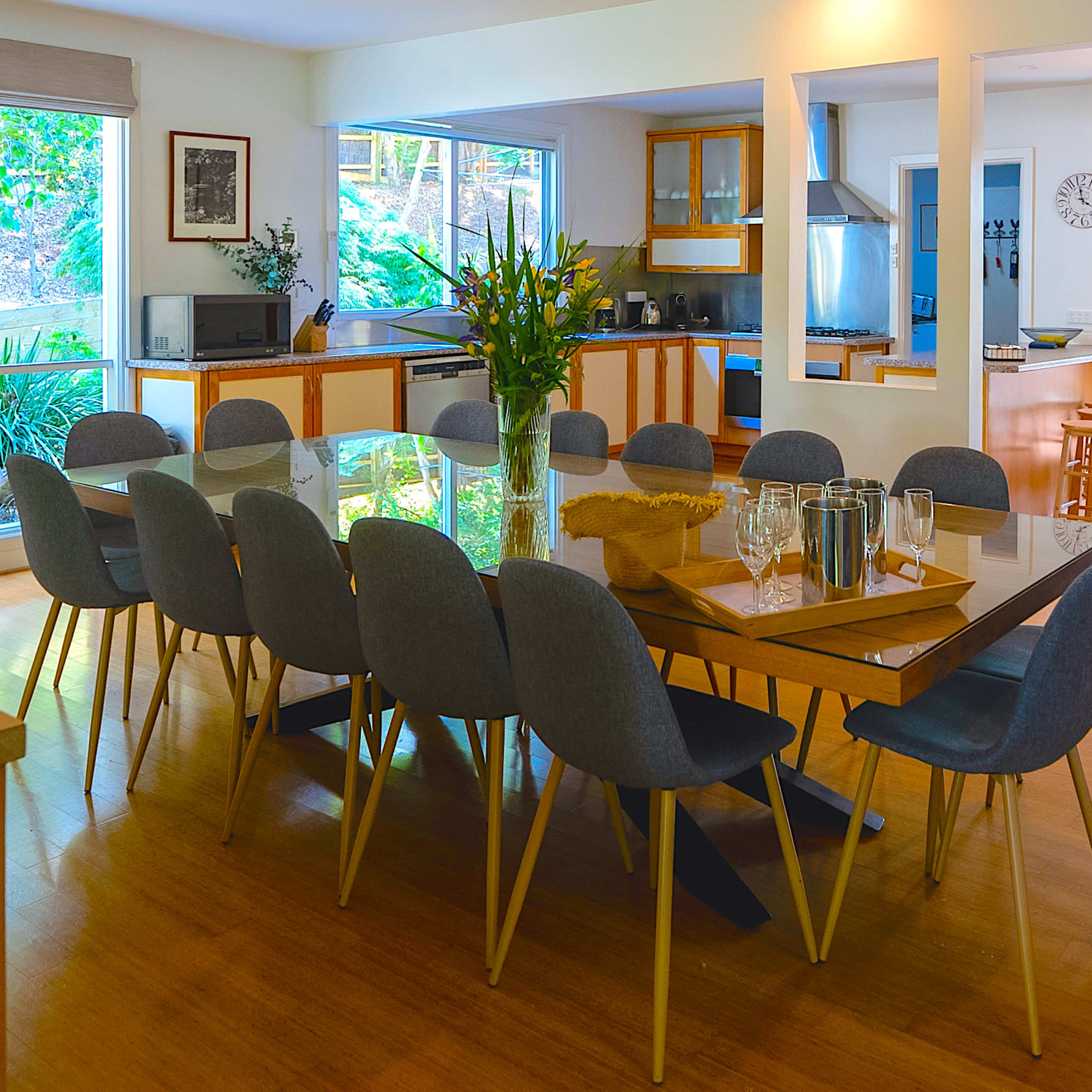 A spacious dining area with a large table surrounded by gray chairs, flanked by a kitchen and sliding glass doors leading to an outdoor space.