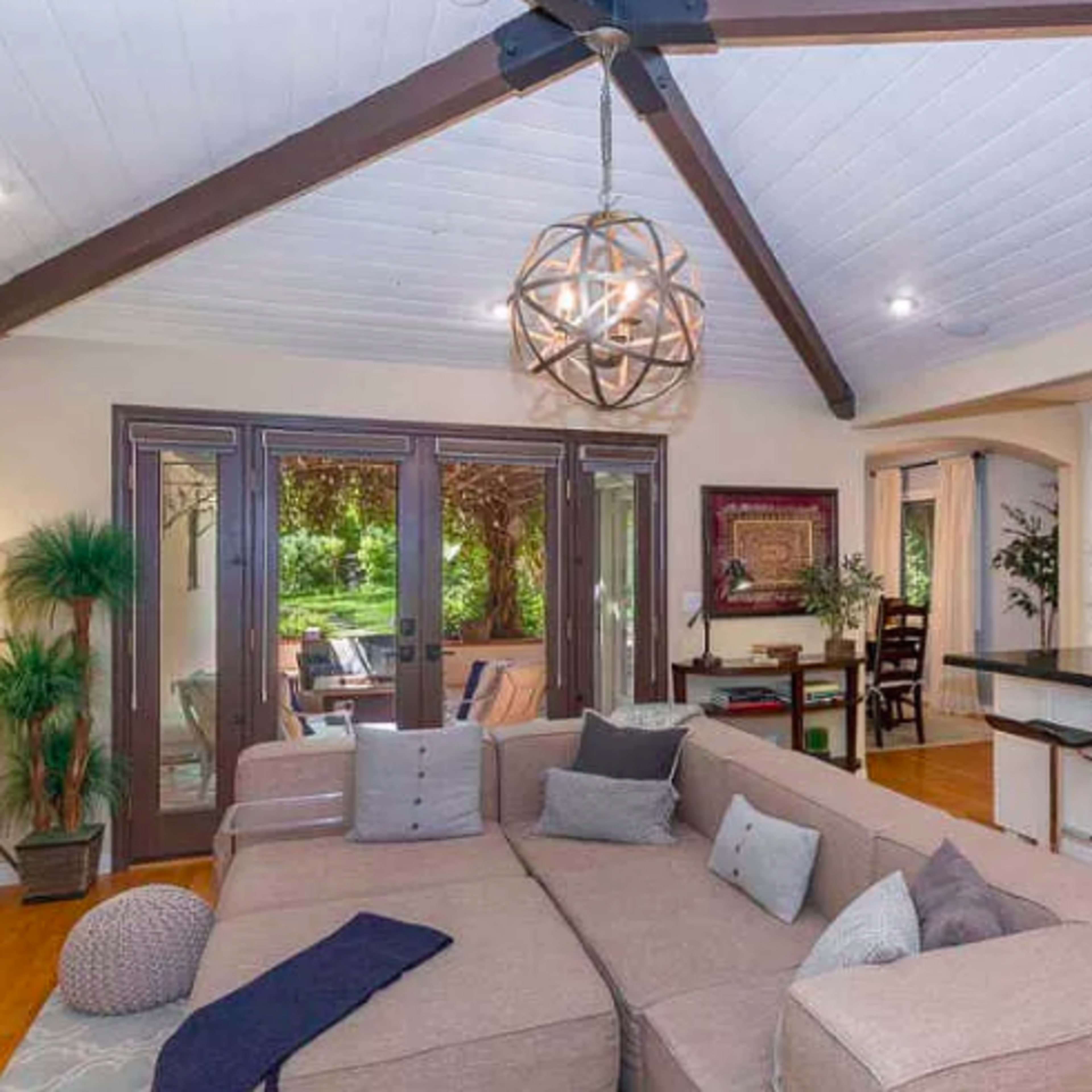 A modern living room features a large sectional sofa, a decorative light fixture, and an open layout that connects to a kitchen area.