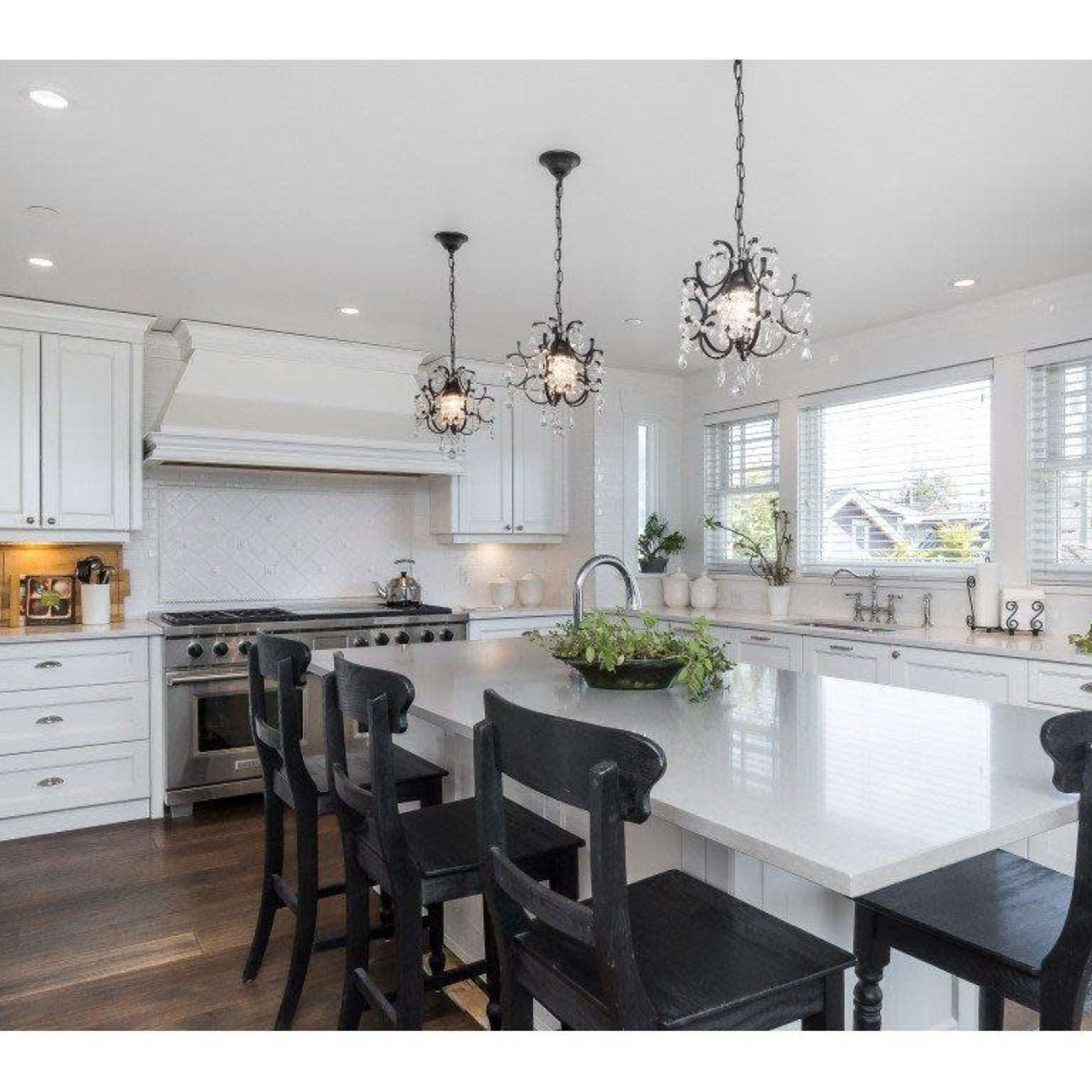 A modern kitchen features a large island with black chairs, white cabinetry, and pendant lighting.