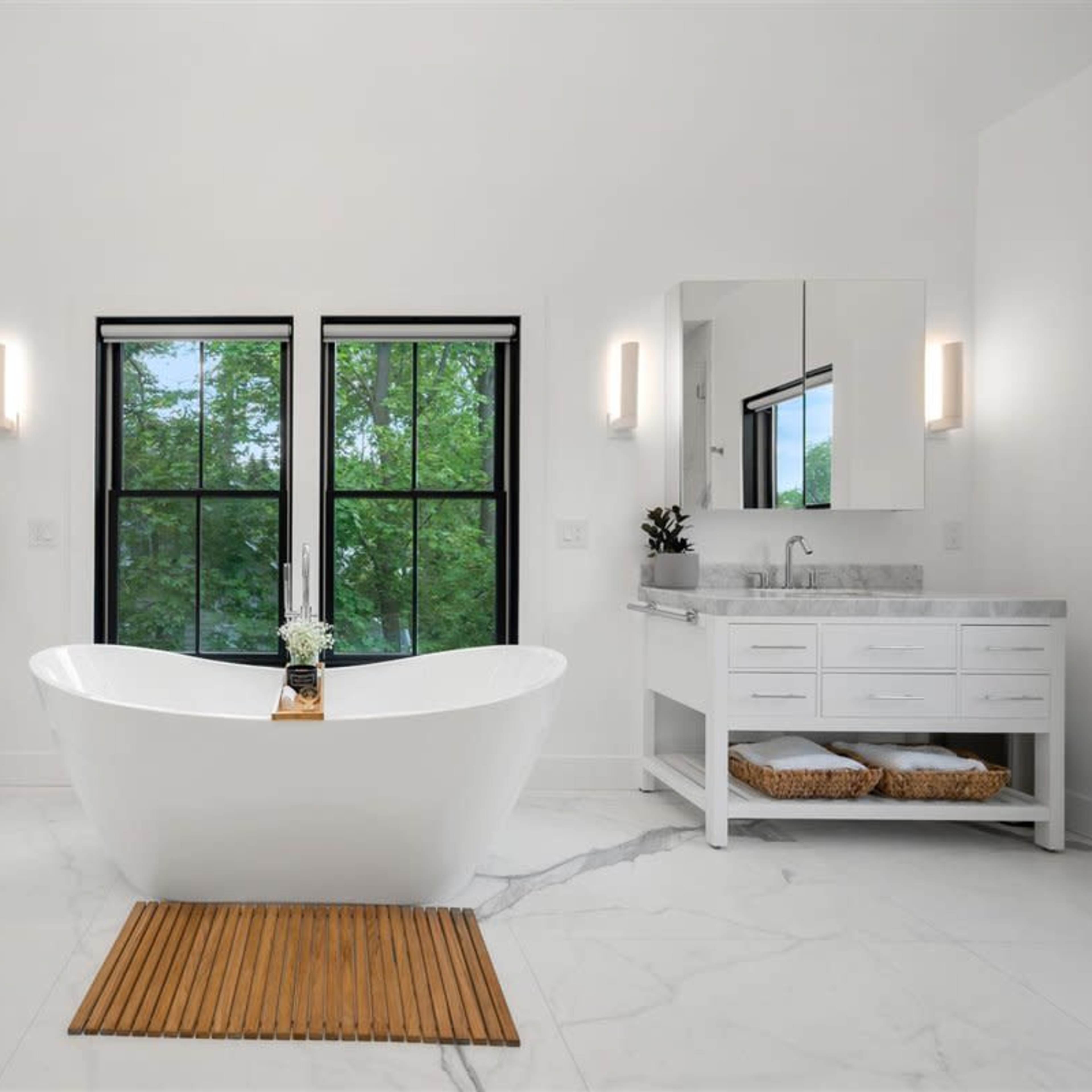 A modern bathroom featuring a freestanding bathtub, dual vanities with mirrors, and large windows overlooking greenery.