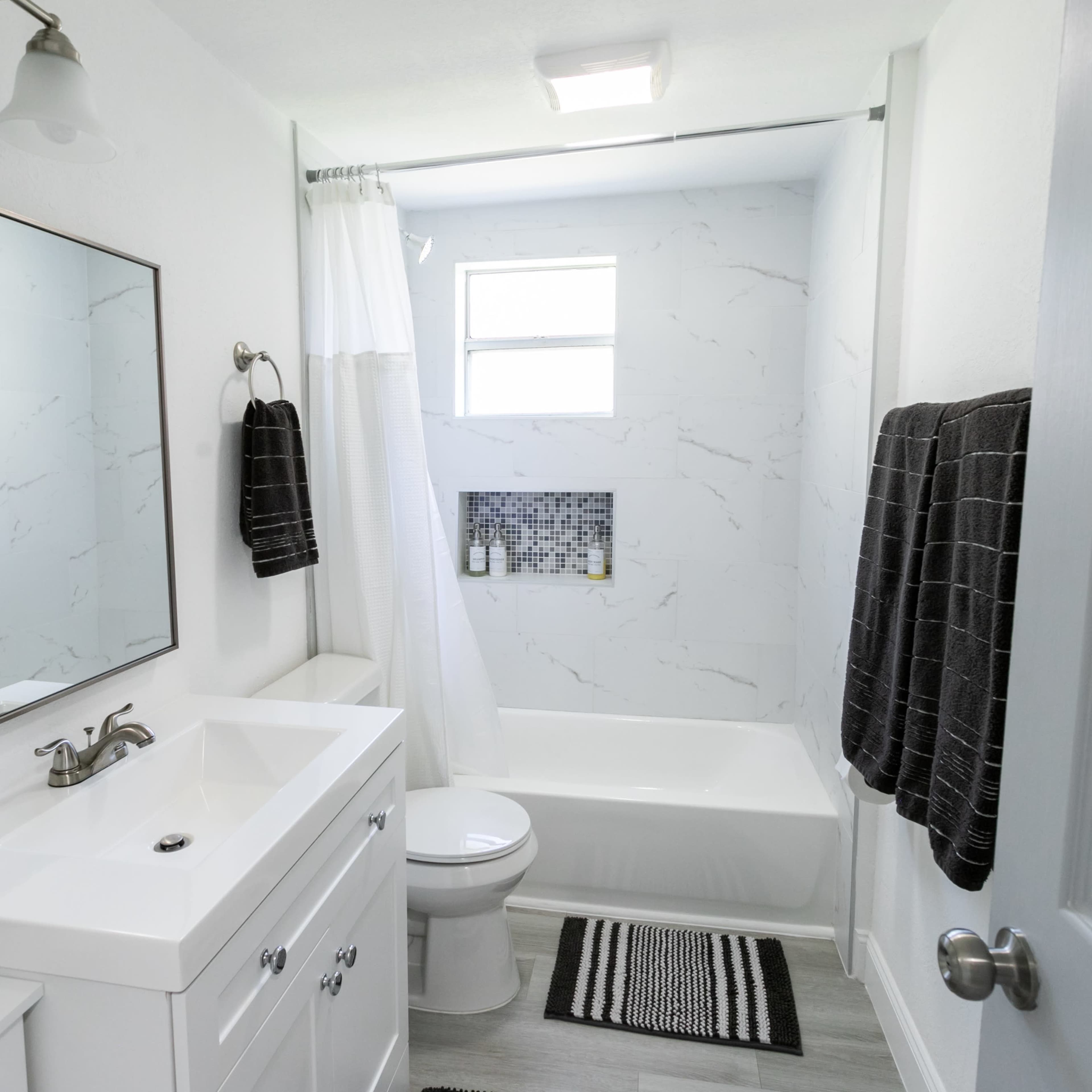 A modern bathroom featuring a white bathtub, a white sink with a mirror, and black towels hanging on a rack.