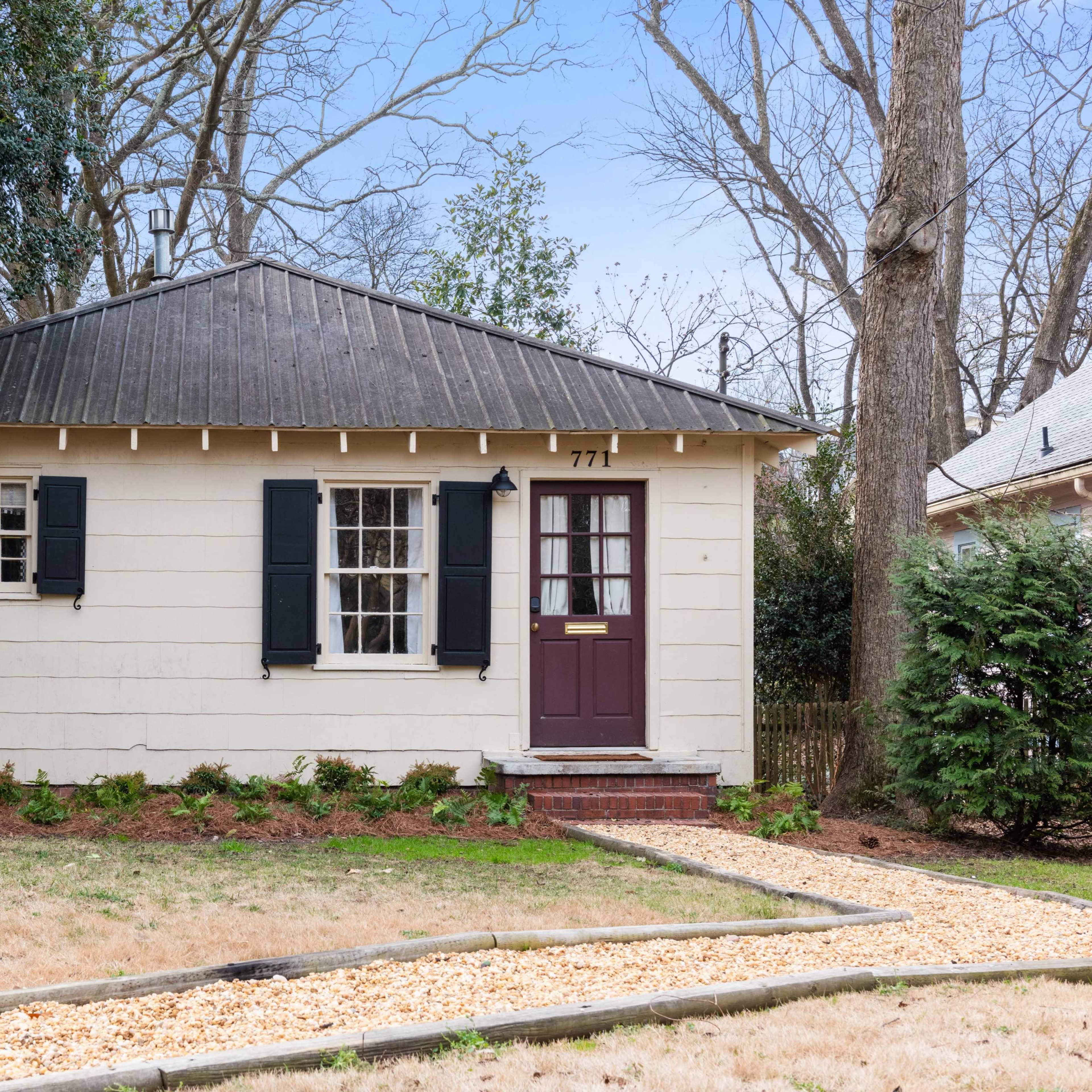 A single-story house with a gabled roof, black shutters, and a pathway lined with gravel leading up to the front door.