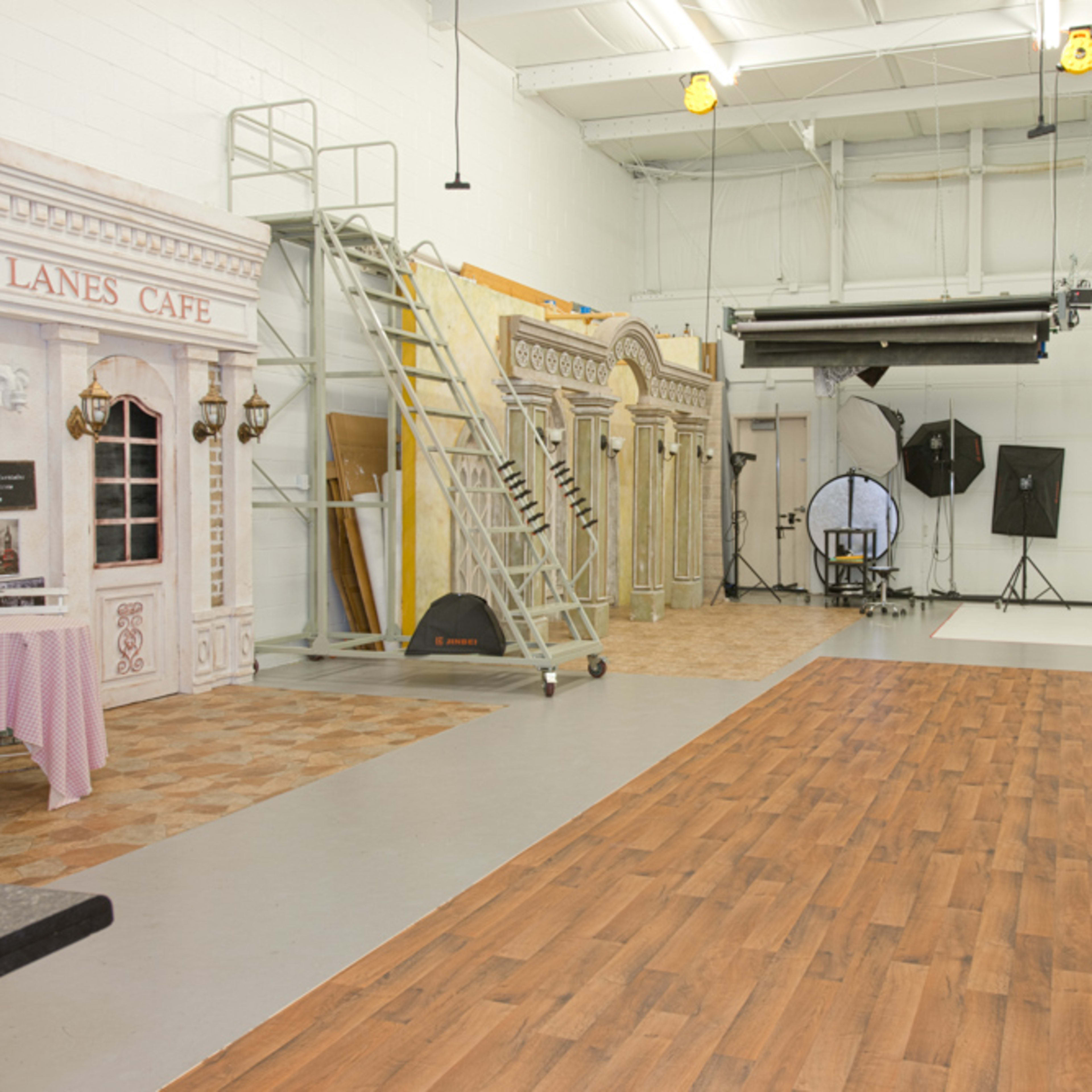 A spacious photography studio with a café setup, a ladder, and various backdrops, including a plain white area for shooting.
