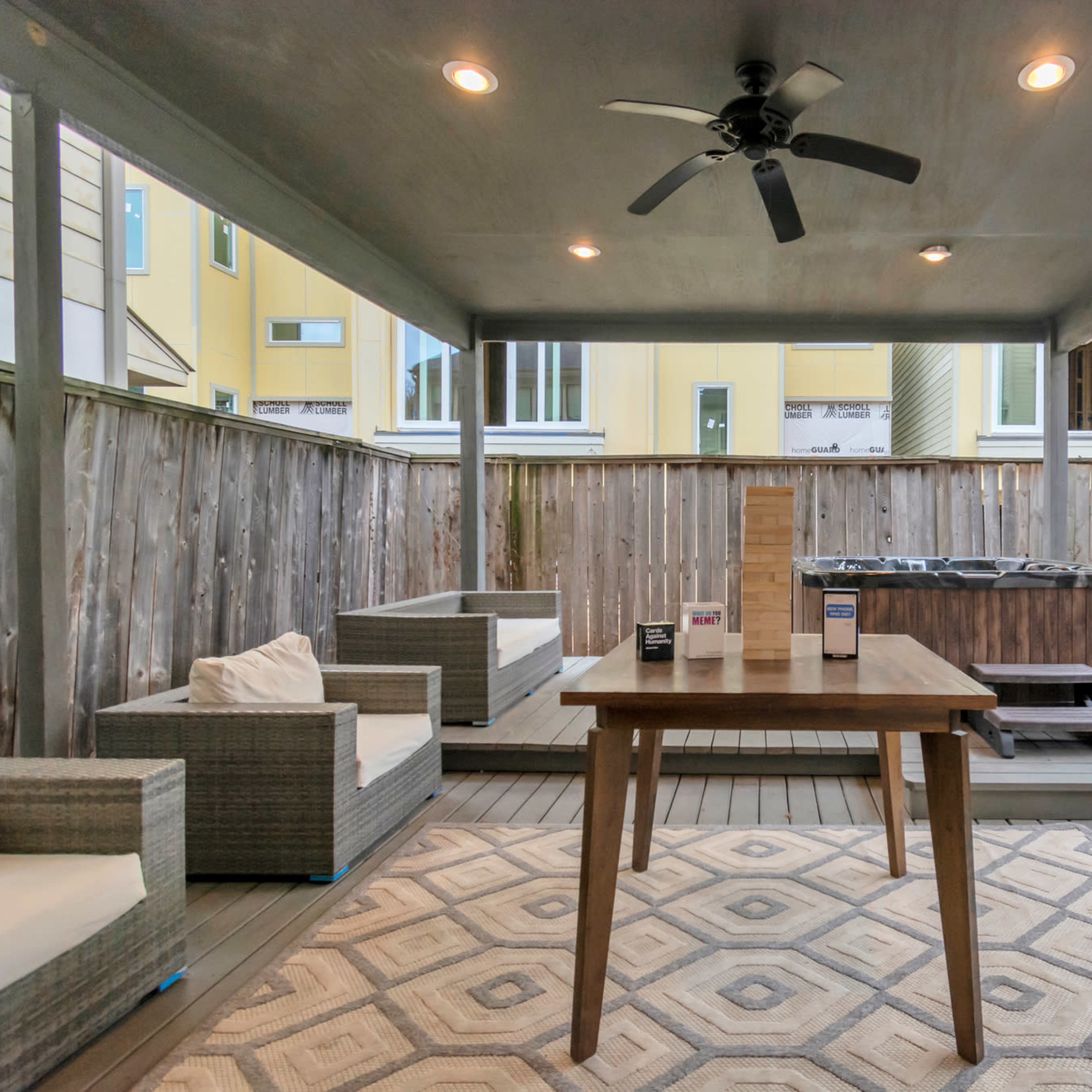 A covered outdoor patio with a table, two couches, and a hot tub surrounded by wooden fencing.