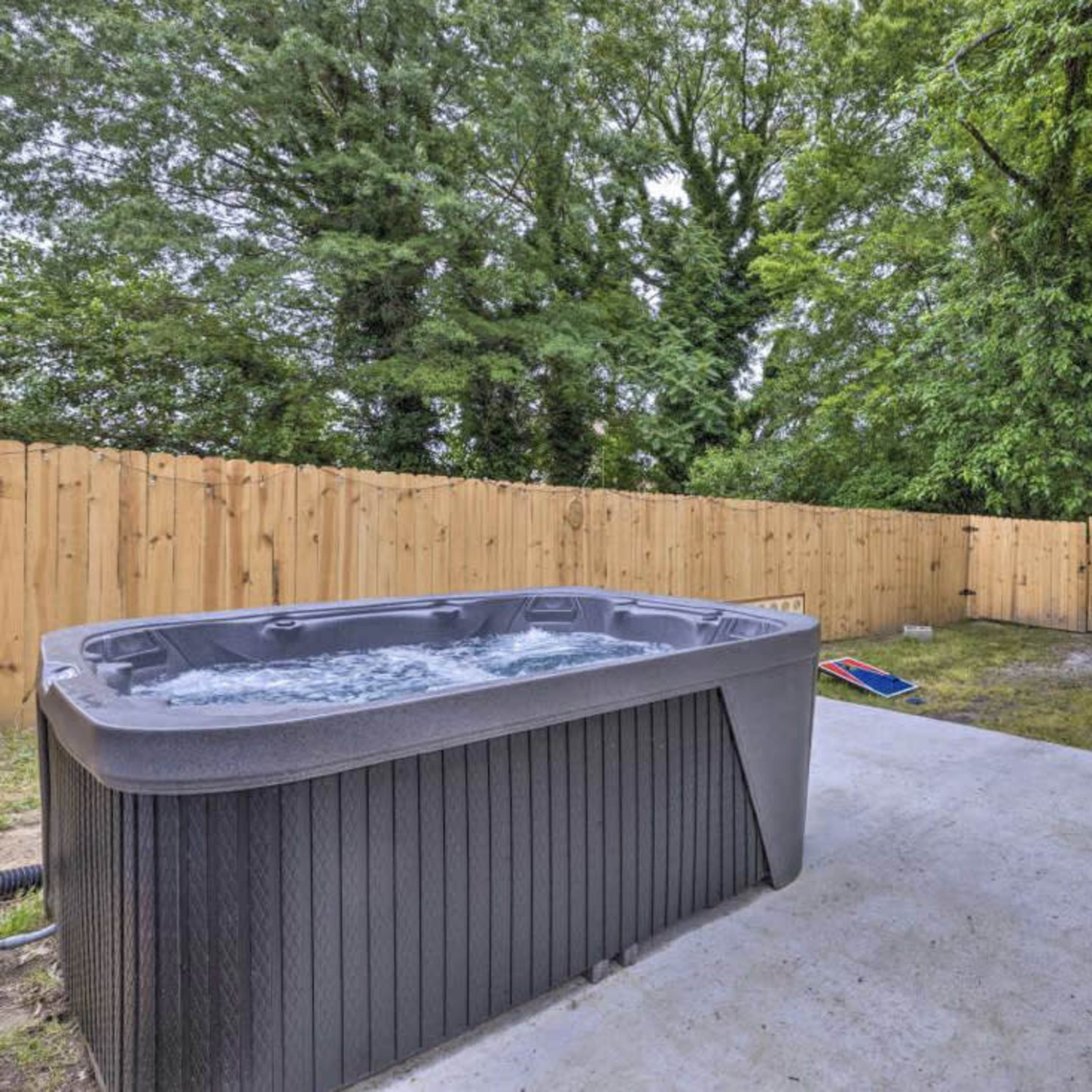 A hot tub sits on a concrete pad surrounded by a wooden fence and tall trees.