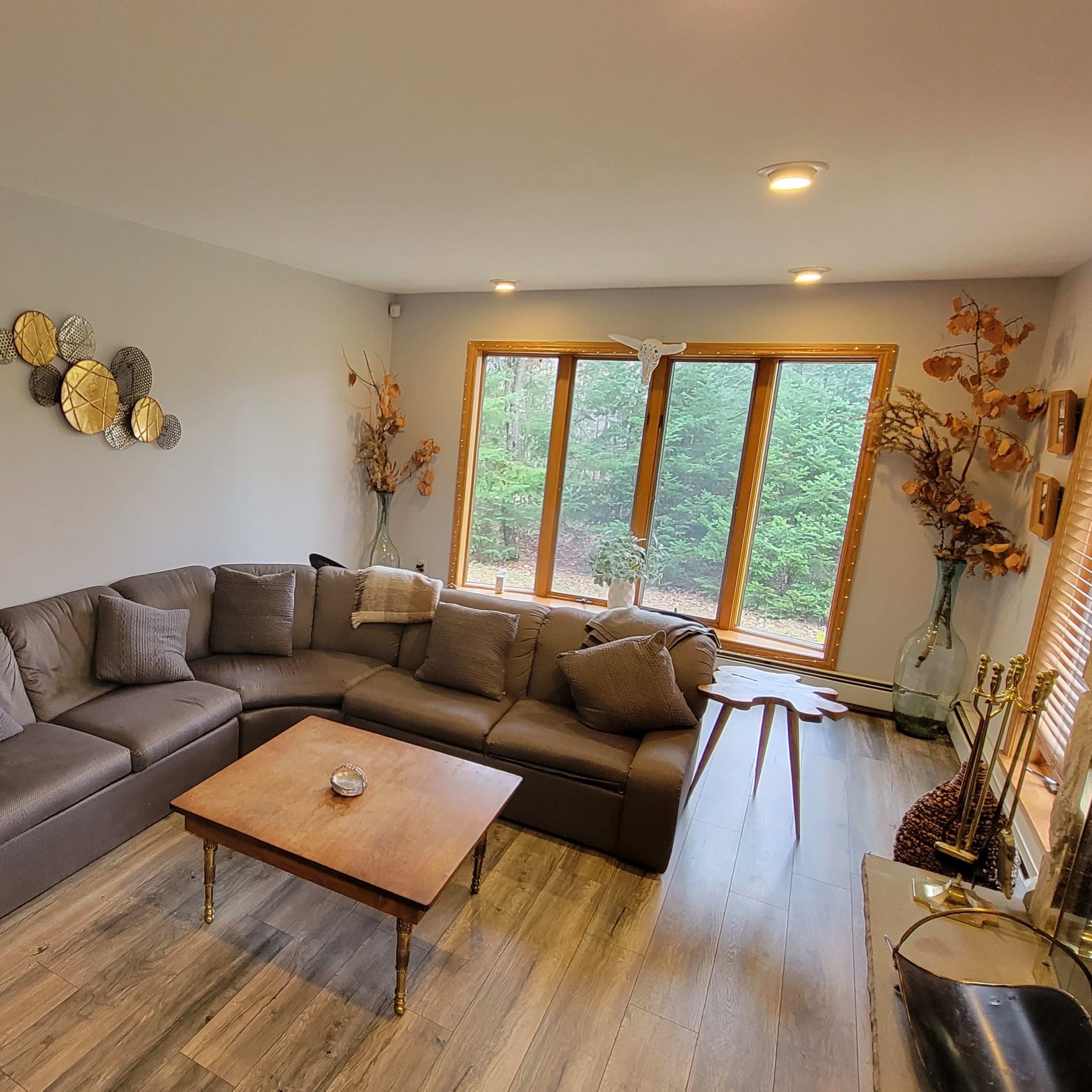A spacious living room features a large sectional sofa, a wooden coffee table, and windows overlooking a natural landscape.