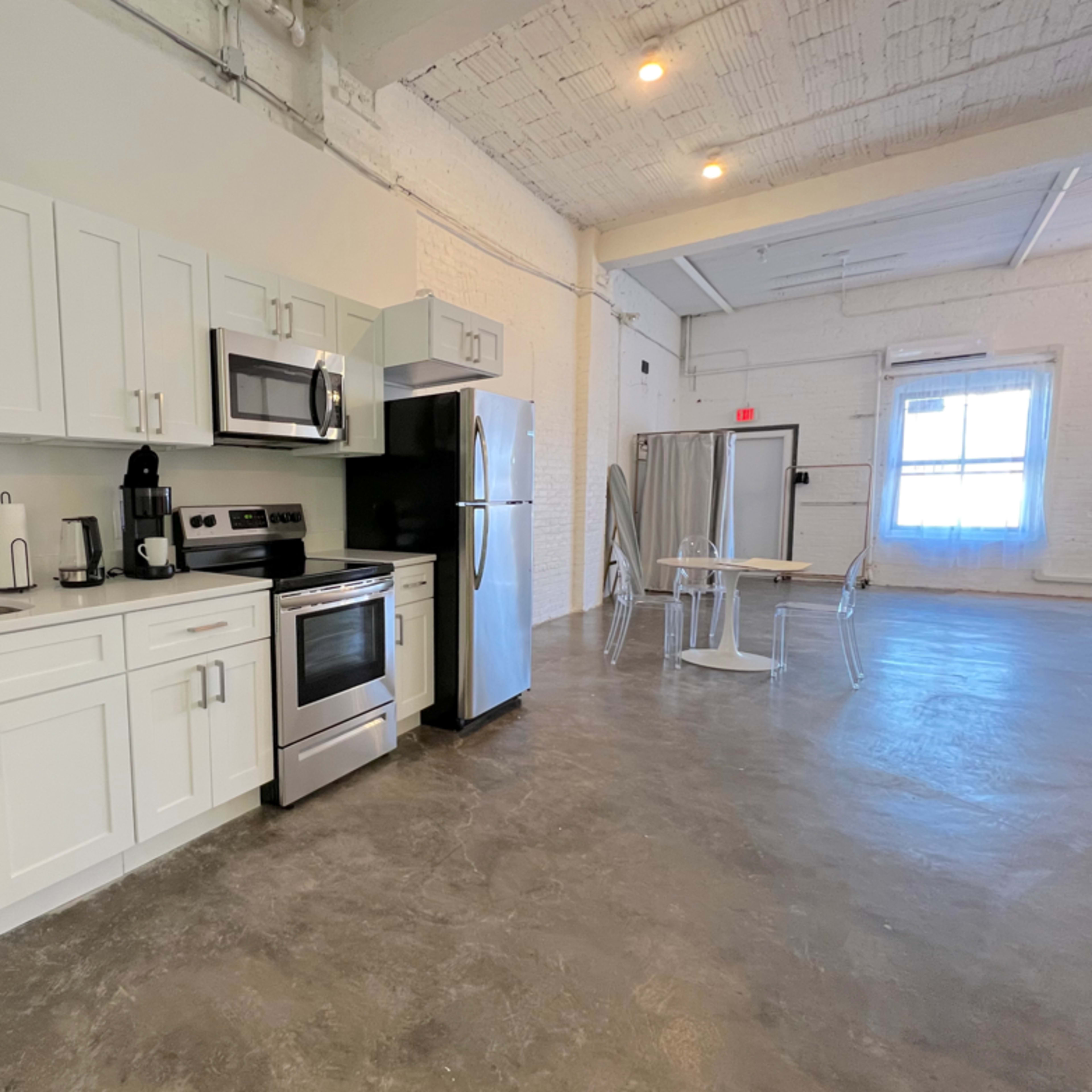 A modern kitchen with stainless steel appliances, white cabinetry, and a polished concrete floor in a spacious, well-lit room.