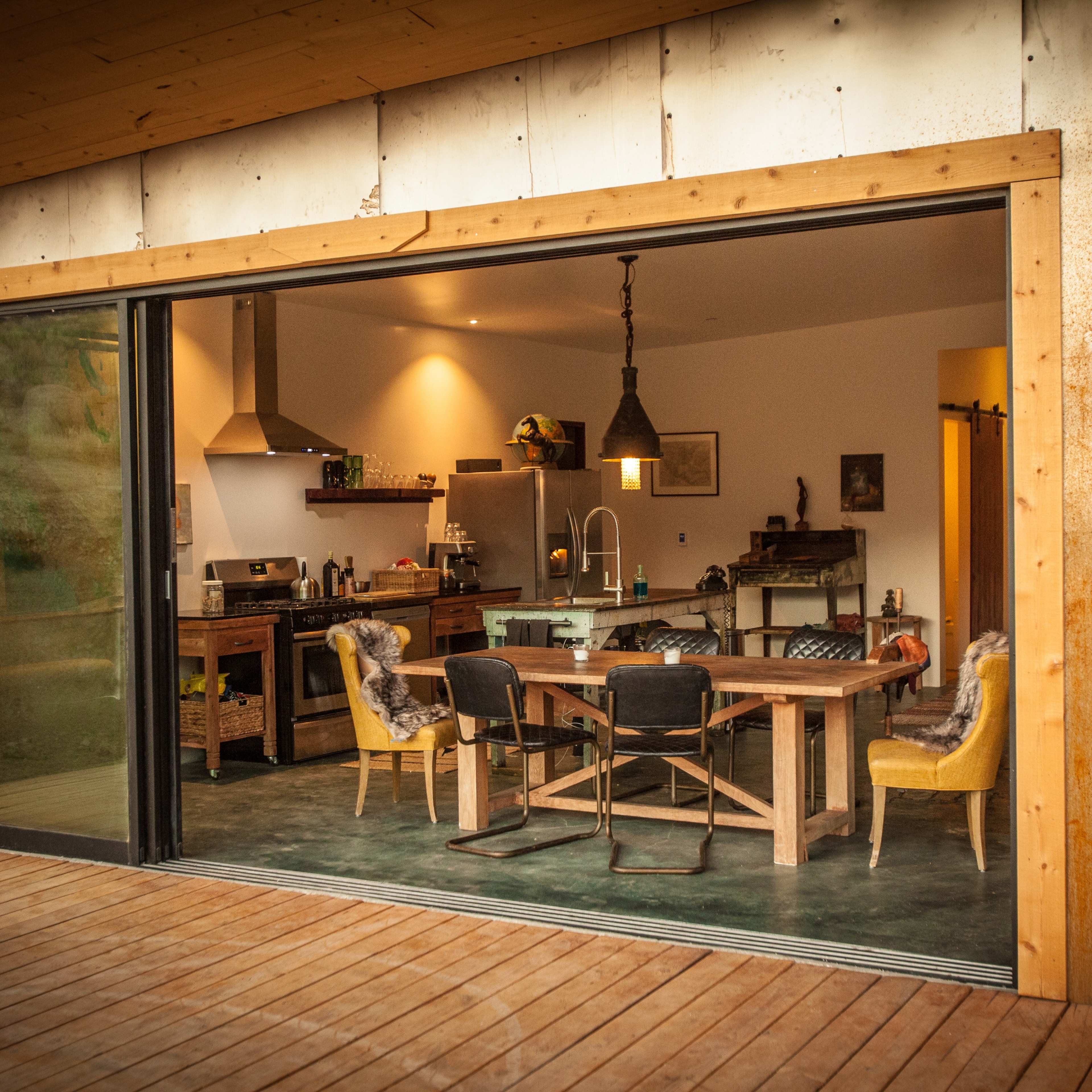 A modern kitchen with wooden walls, a large dining table, and a sliding glass door that opens to a wooden deck.