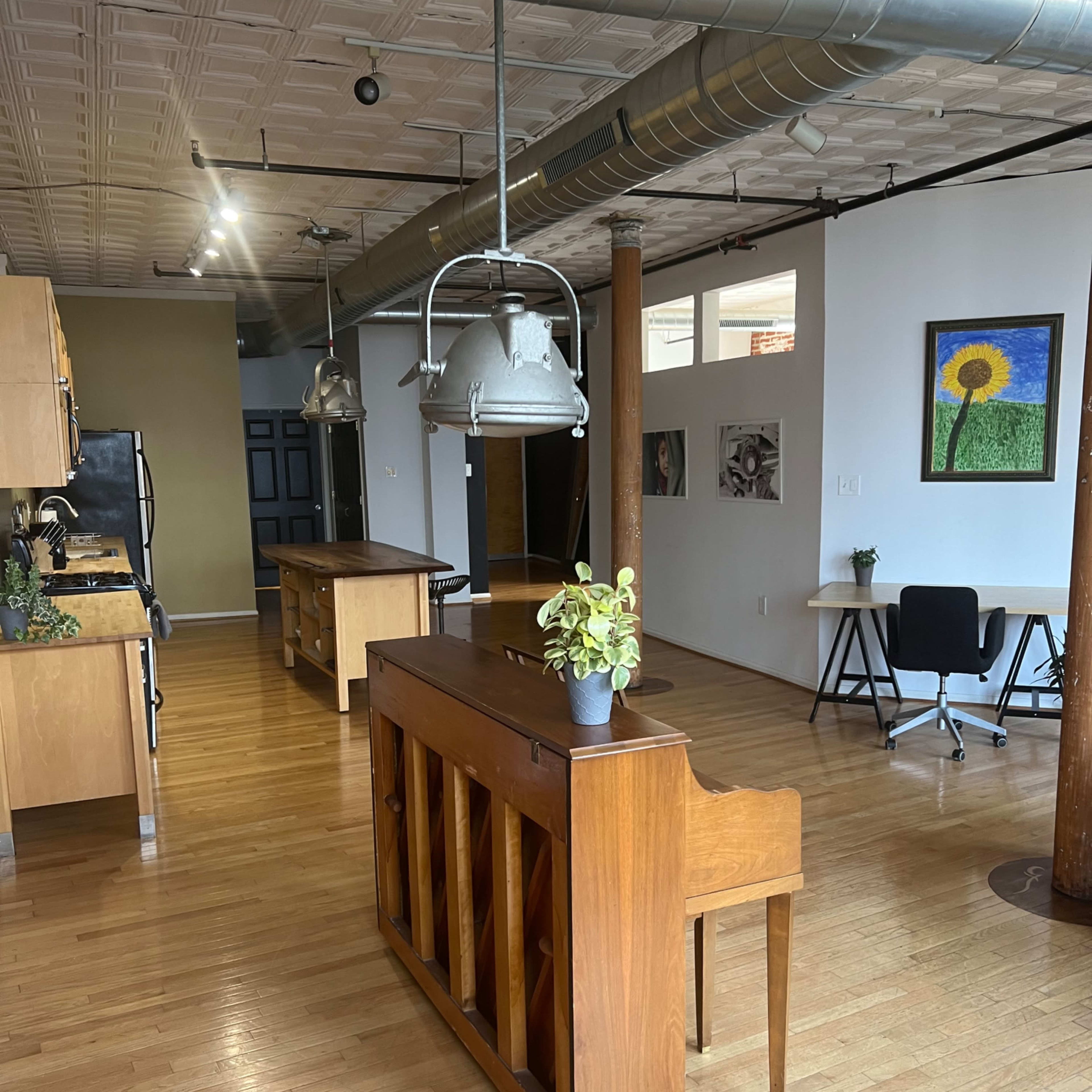 A spacious, modern kitchen and living area featuring hardwood floors, a vintage wooden piano, and various furnishings including a plant and desk.
