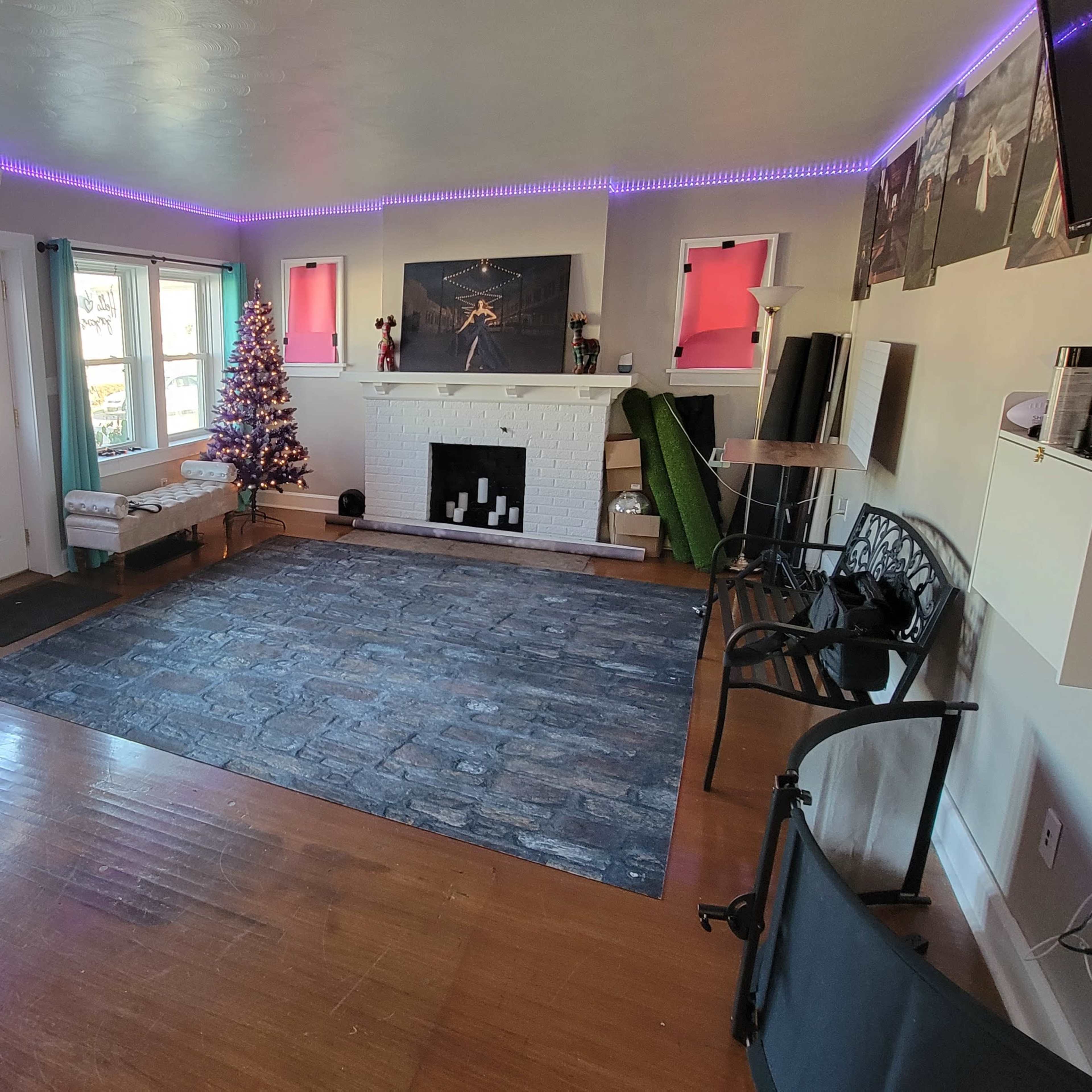 A spacious room with a hardwood floor, decorated with a Christmas tree, a large decorative rug, and various seating and storage areas.