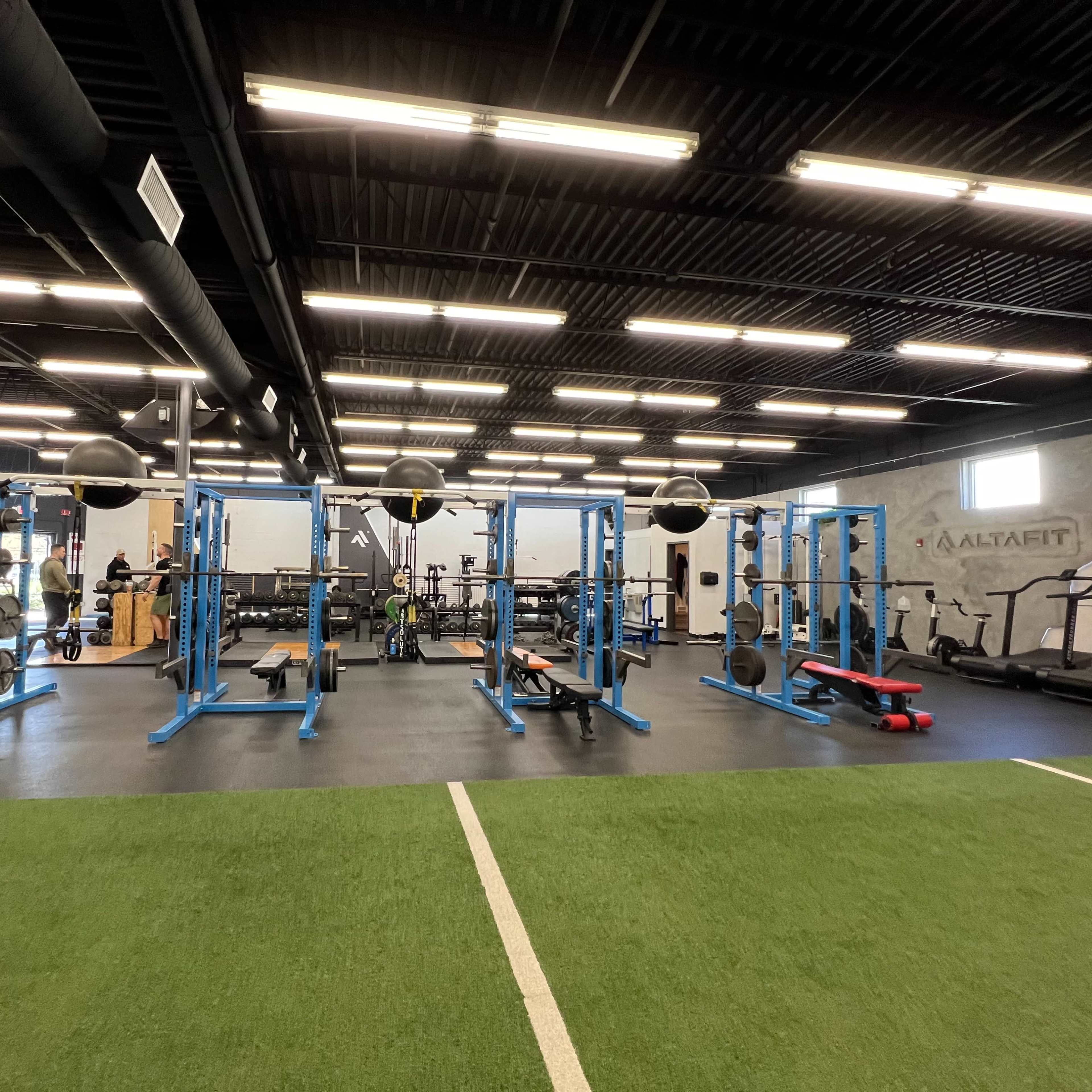 A gym interior featuring blue weightlifting equipment, treadmills, and a turf area.